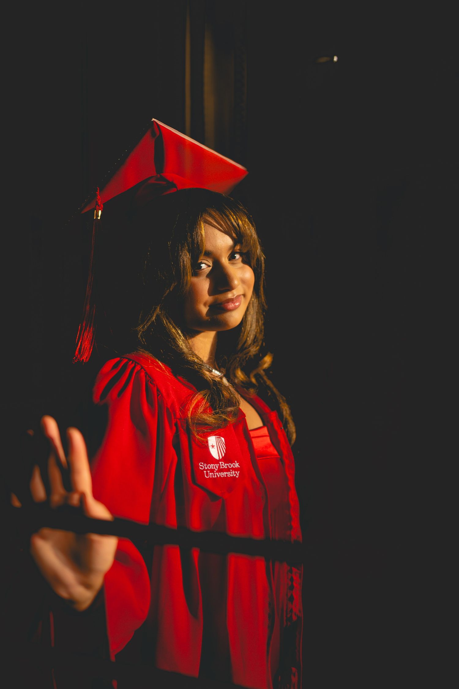 Graduate in red cap and gown poses dramatically in low-key lighting.