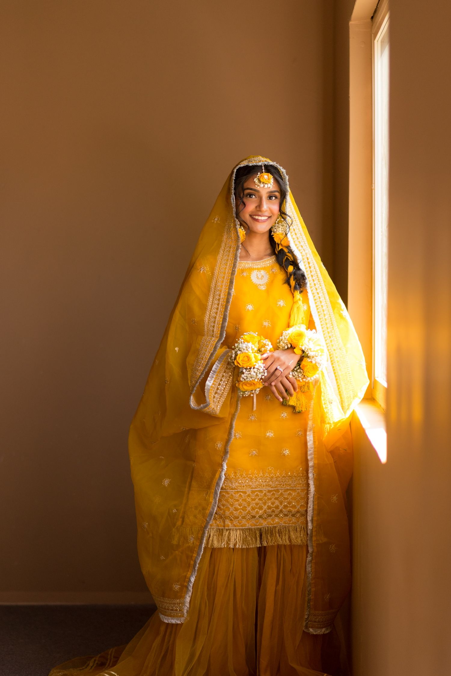Traditional Indian bridal portrait in warm yellow attire with golden light streaming through window.