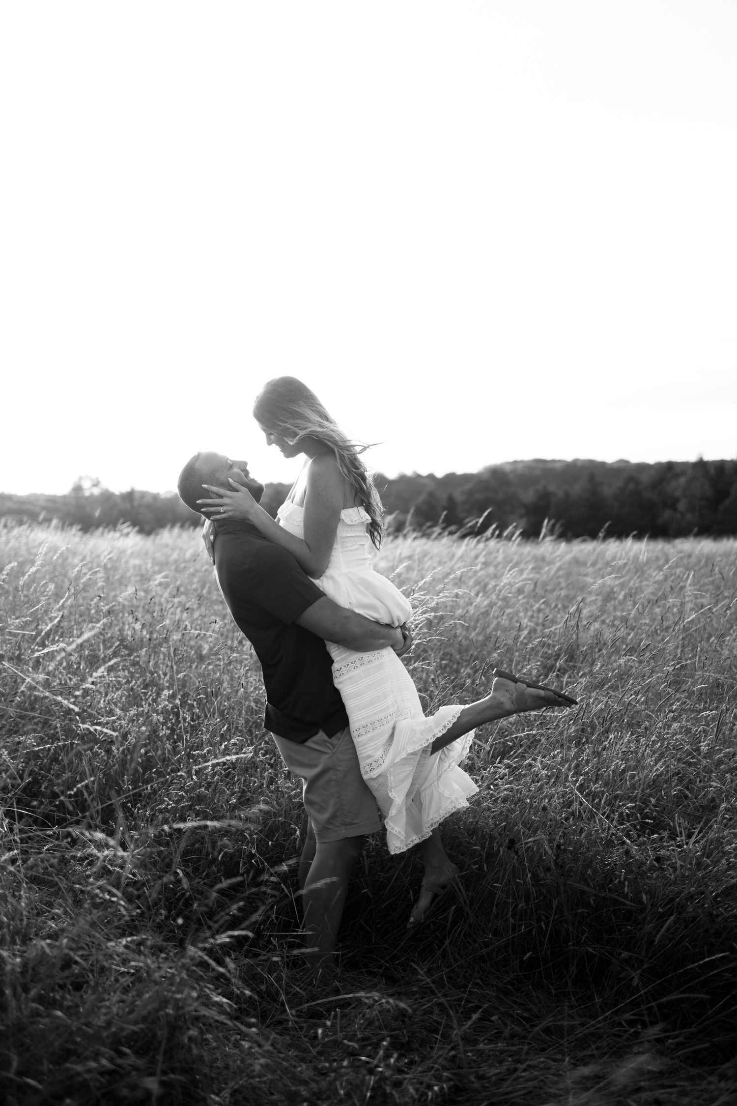 Black and white portrait of couple in romantic lift pose in grassy field.