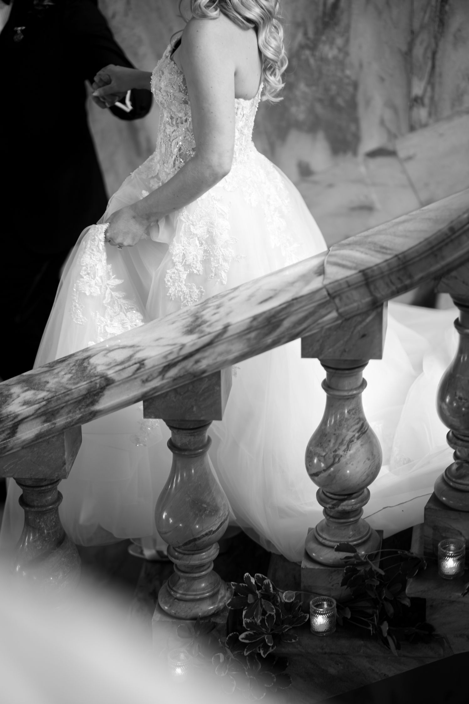A bride in a white wedding dress descends an ornate staircase in a dramatic black and white photograph series.