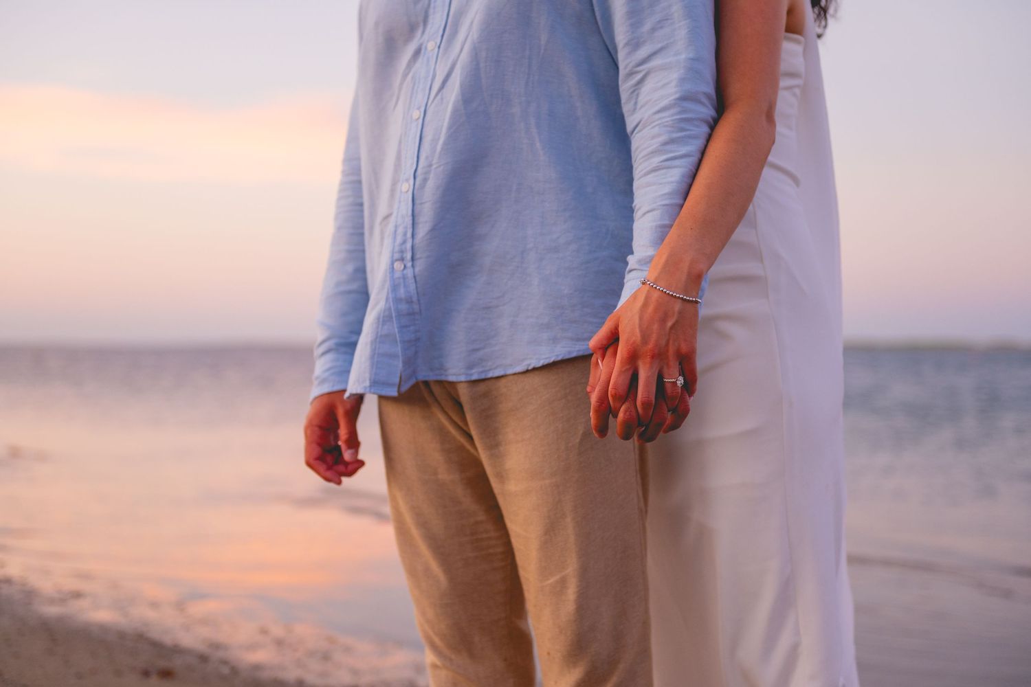 Close-up view of a couple holding hands at sunset on a Cape Cod beach.