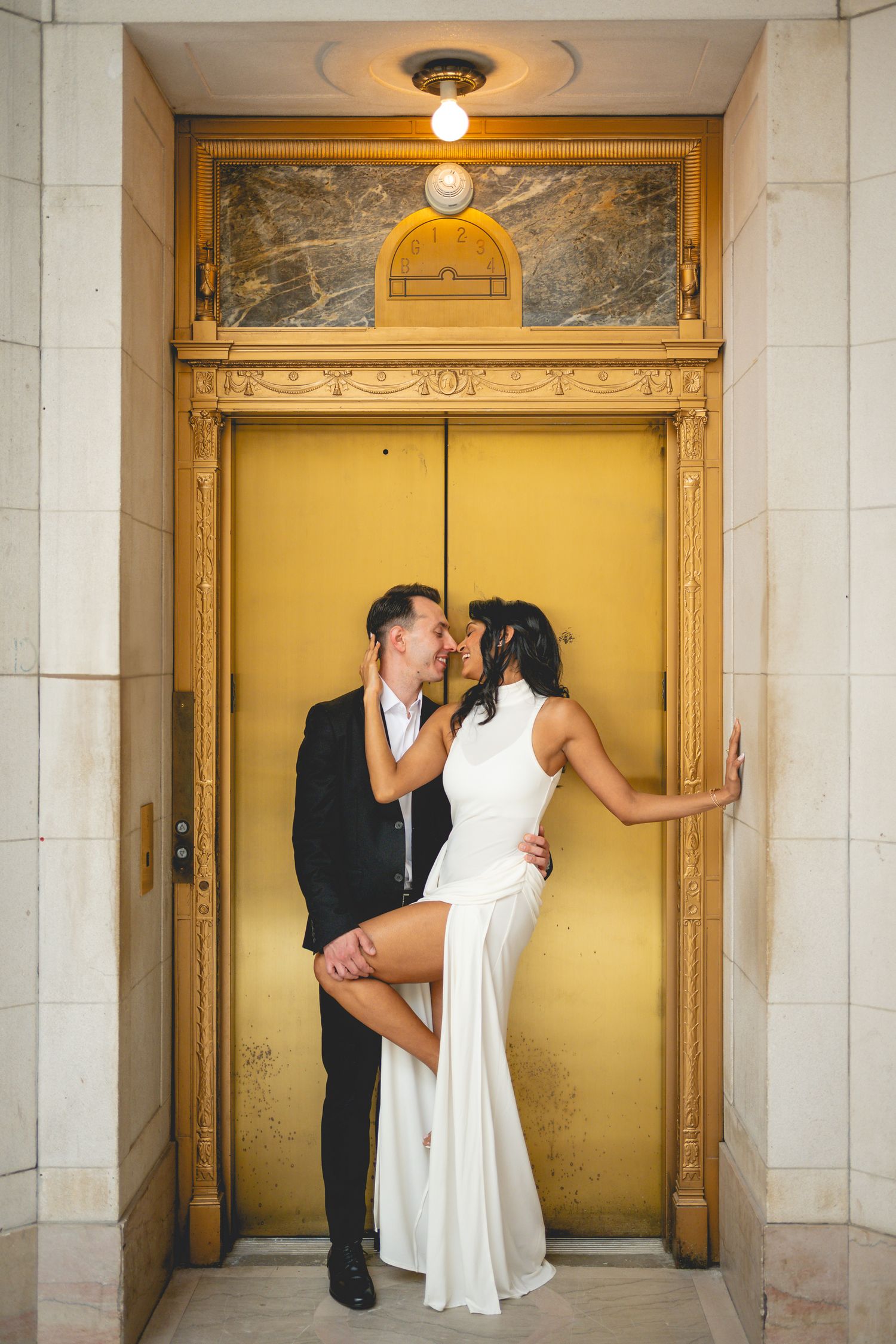 A couple poses dramatically against a golden elevator door in formal attire at Hartford City Hall.