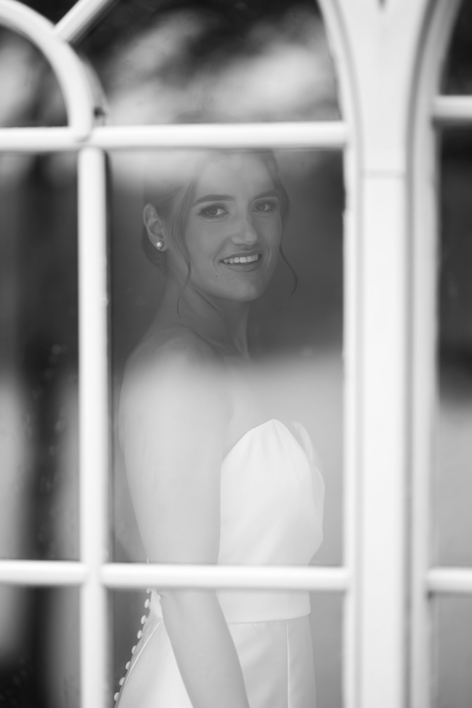 Black and white photo through window panes showing wedding dress details.