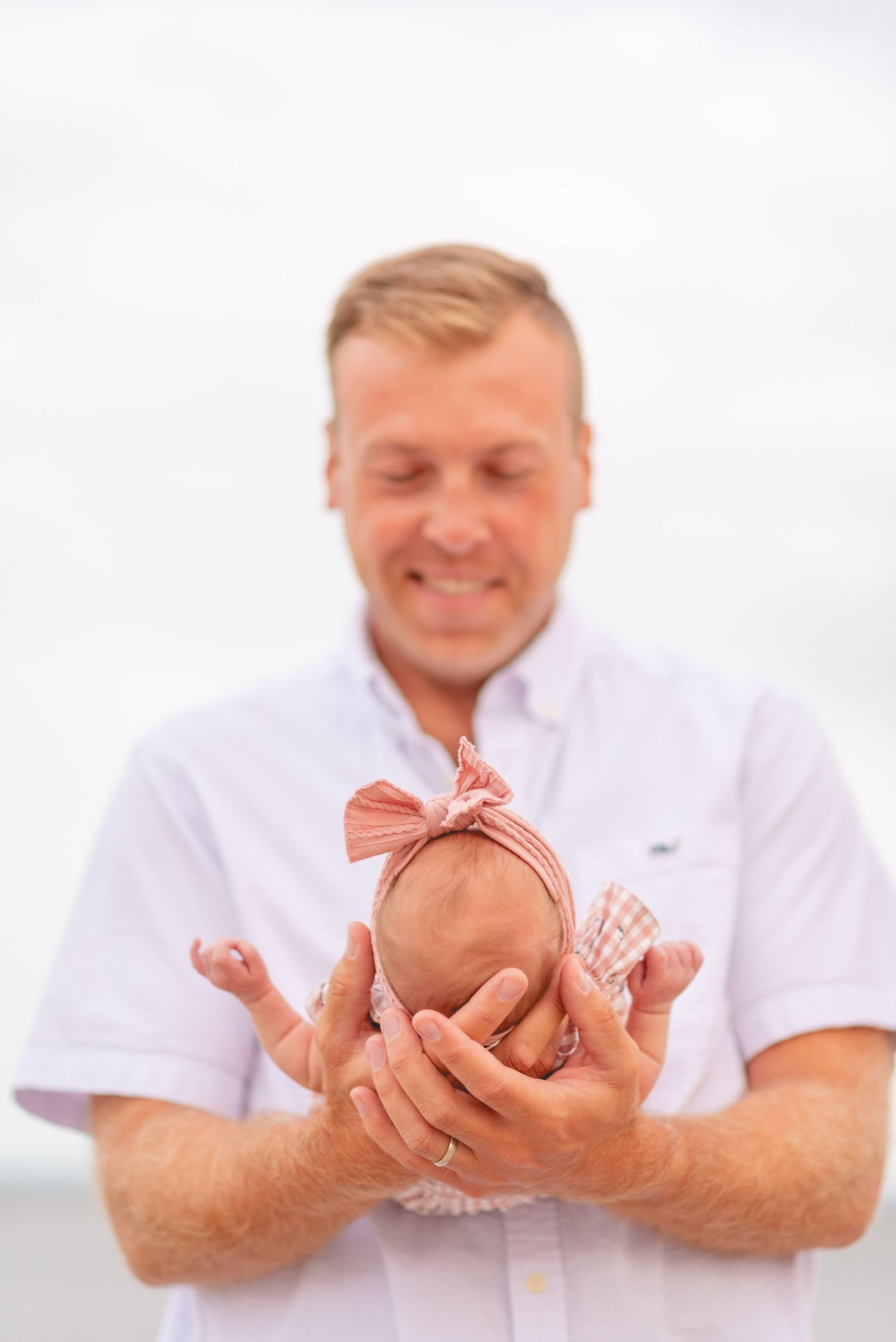 Gentle hands cradle and support a small baby in white.