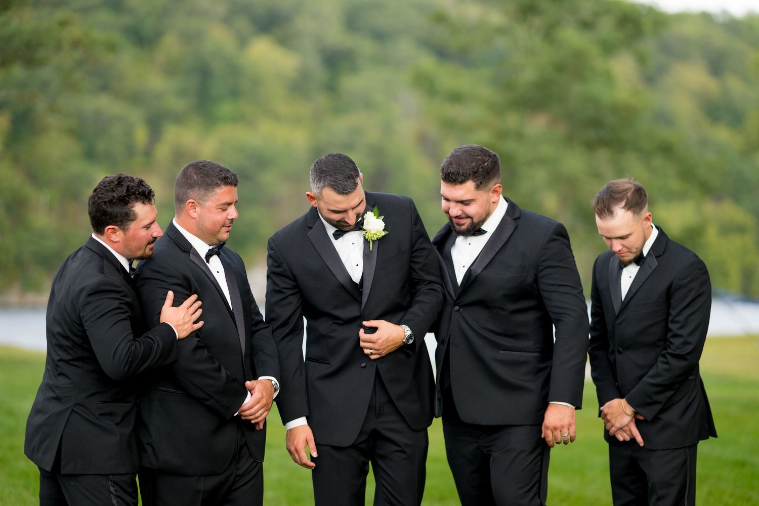 Groomsmen in black suits share a lighthearted moment outdoors.