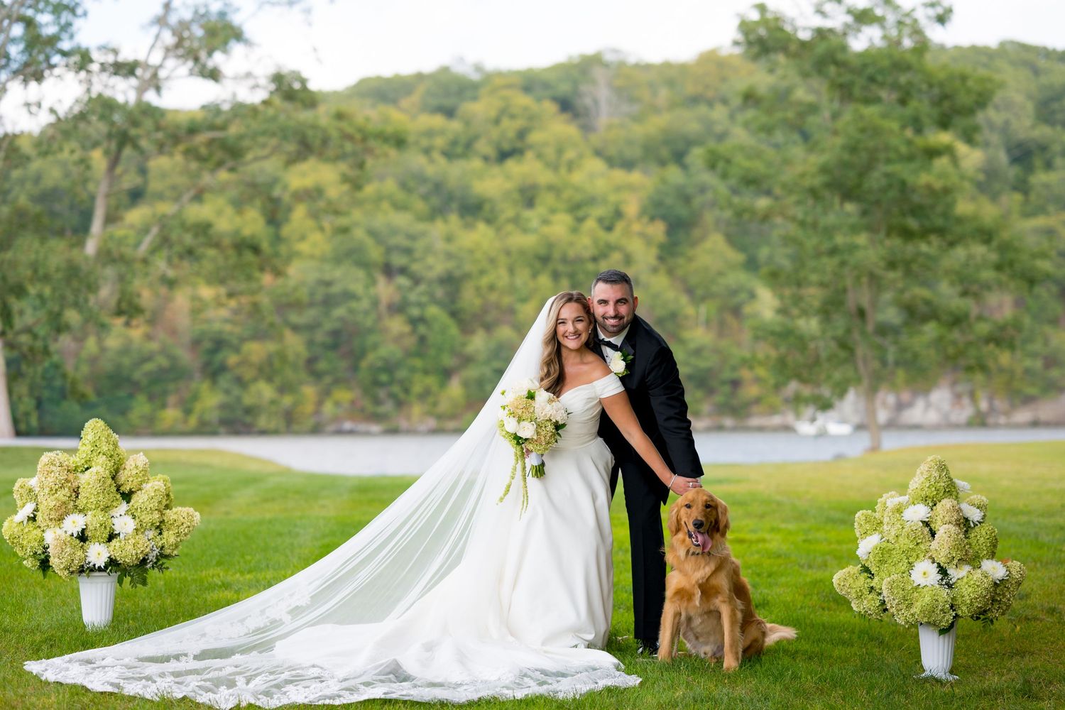 Wedding couple and their dog pose for photos with floral arrangements outdoors.
