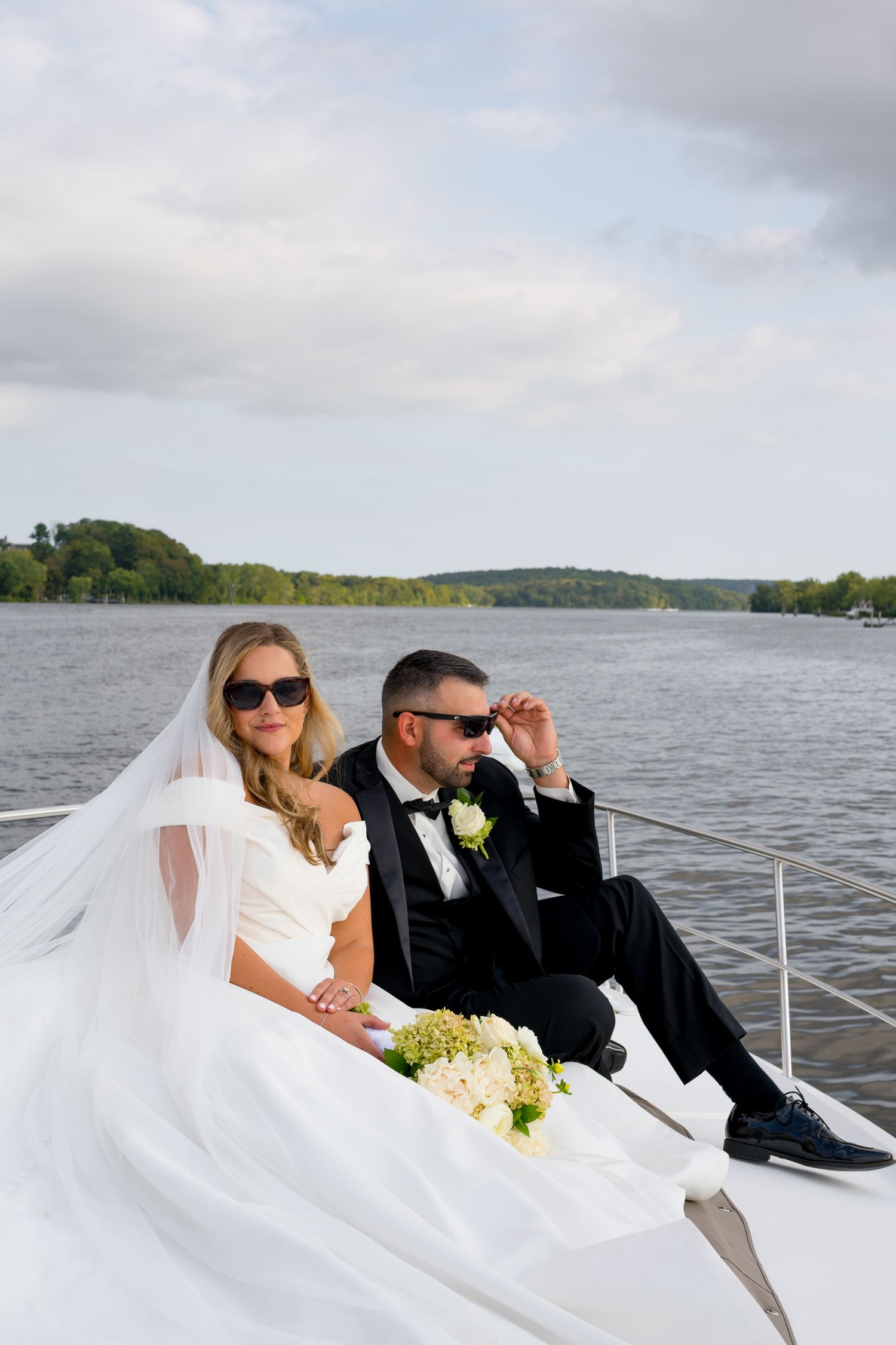 A wedding couple relaxes on a boat with a scenic lake view in the background.