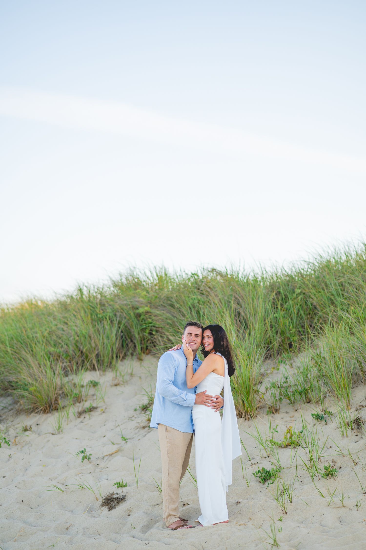 Couple standing together on sandy dunes with beach grass at Chatham Lighthouse Beach in Chatham, Massachusetts.