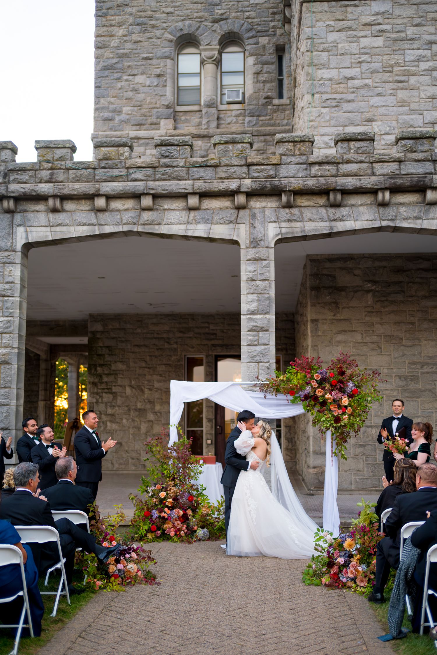 An outdoor wedding ceremony setup with stone architecture and colorful floral arrangements under an elegant white canopy.