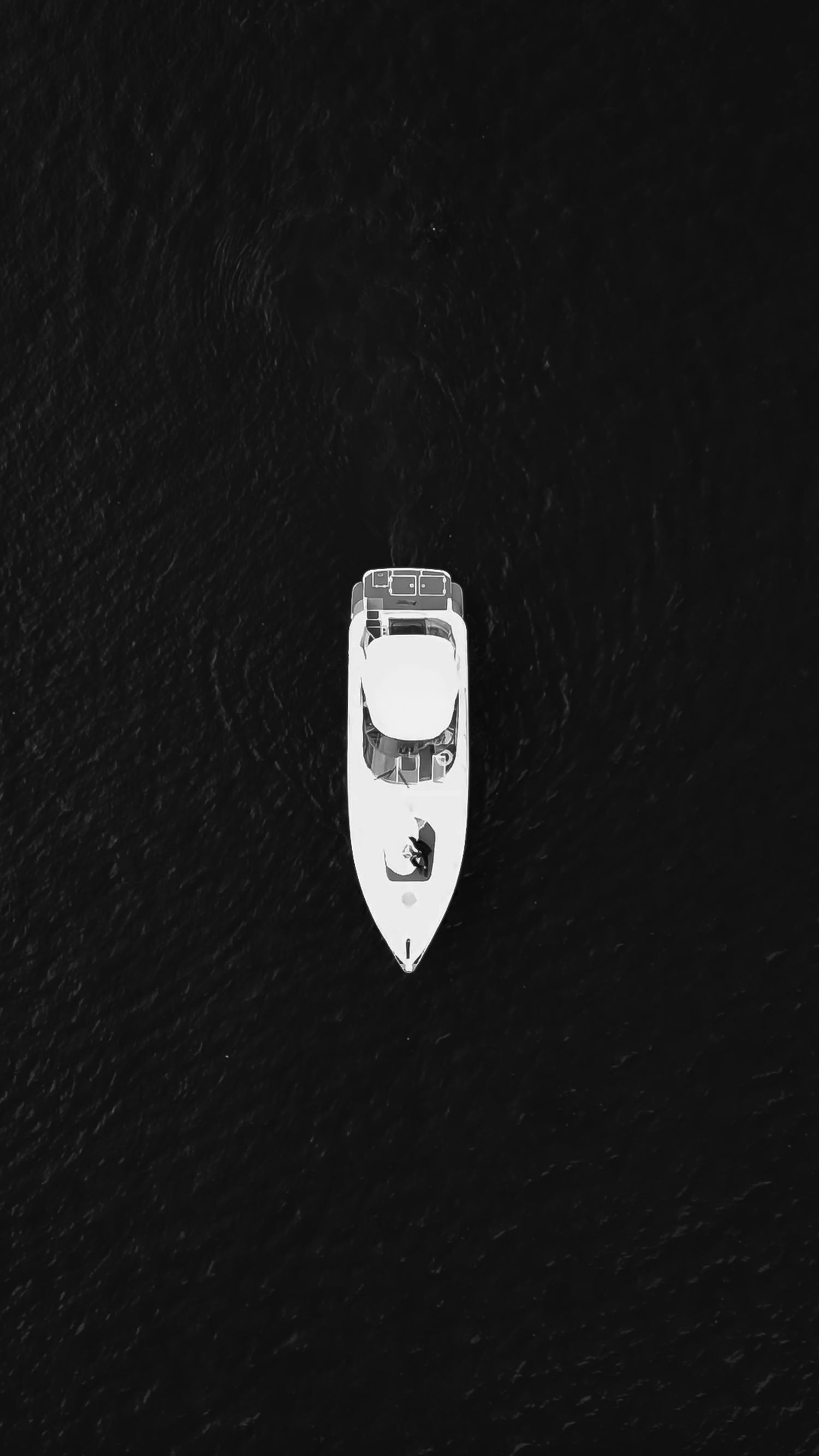 Aerial view of a white speedboat cruising through dark waters.