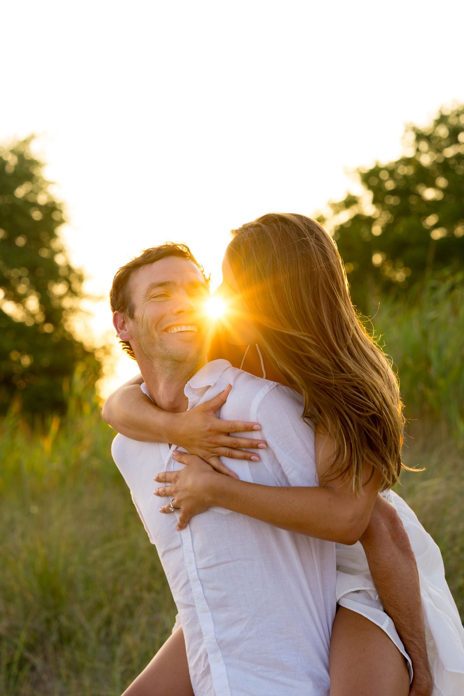 A joyful embrace captured during golden hour with sunlight streaming through trees in the background.
