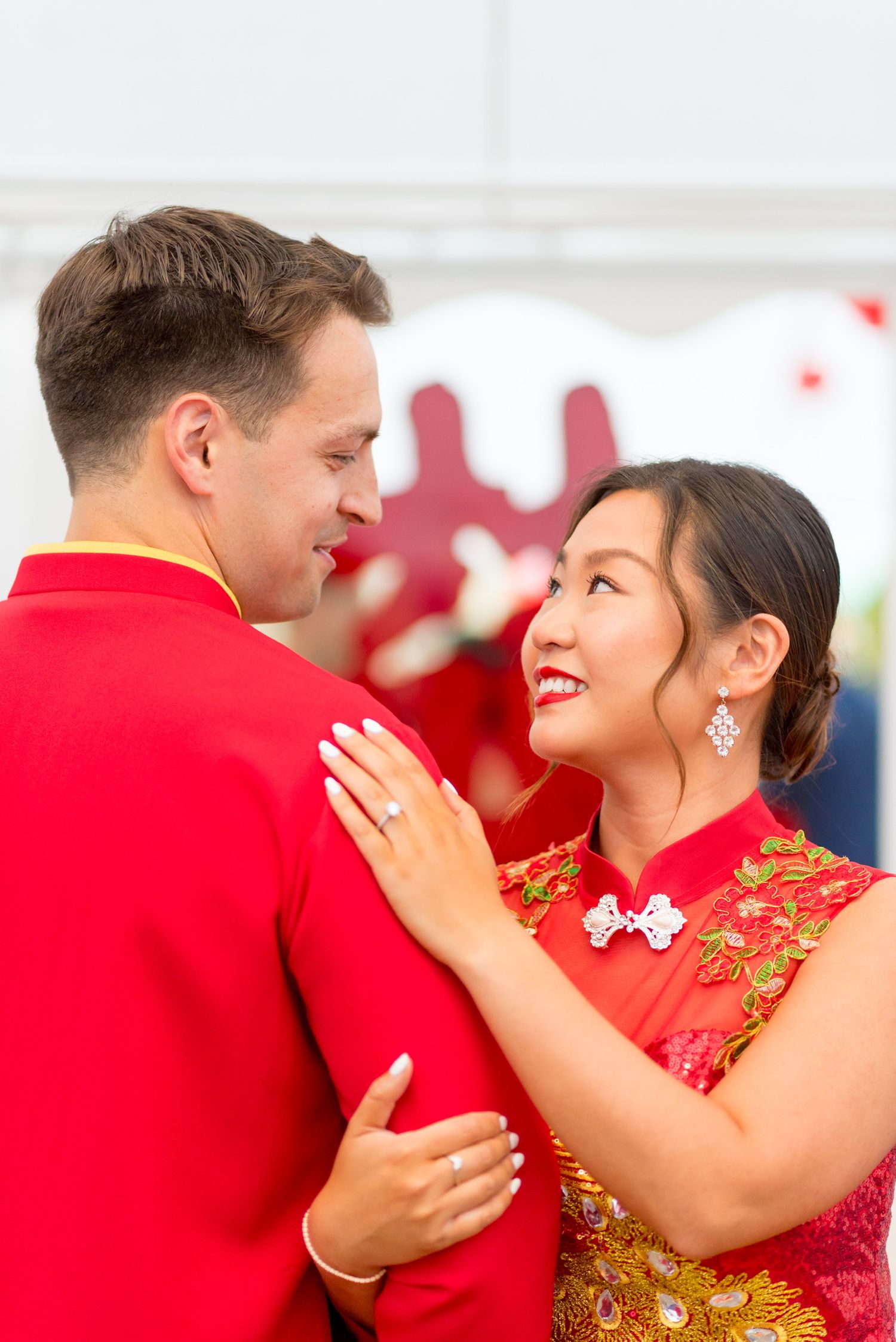 Couple shares intimate moments wearing red and gold traditional tea ceremony attire during celebration in Connecticut.