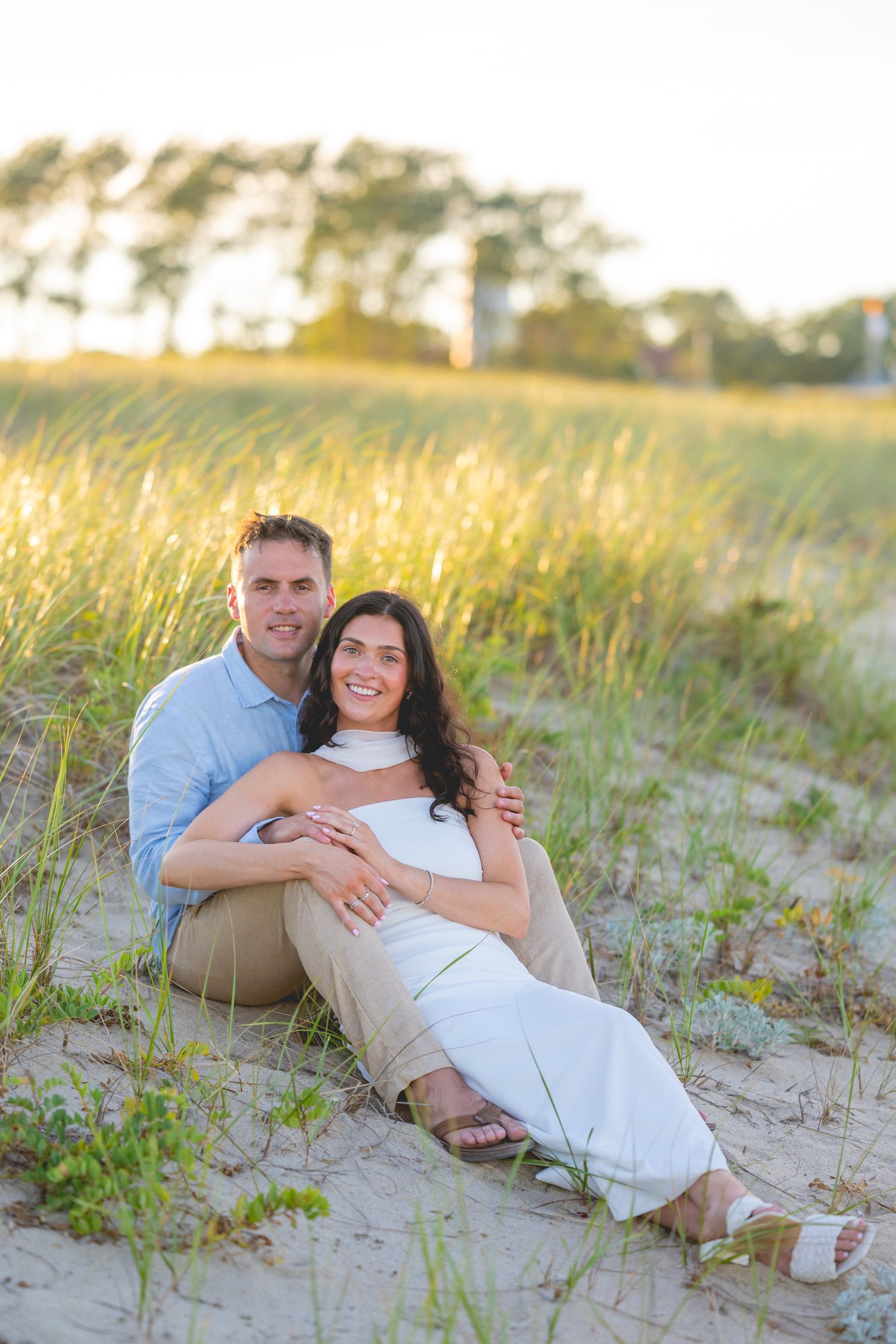 A couple relaxes together on sandy Cape Cod beach dunes during golden hour.
