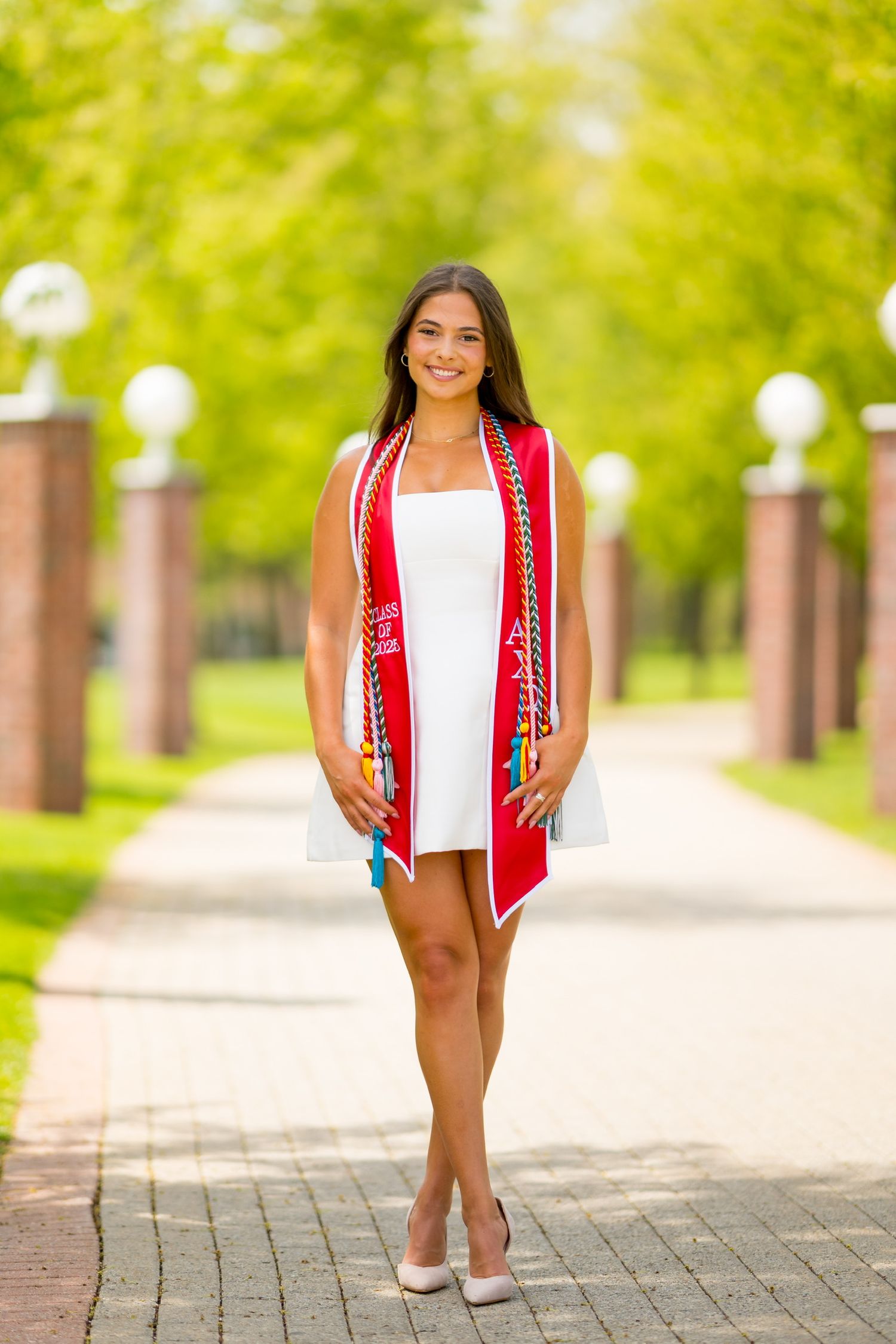 Quinnipiac University graduate poses on campus pathway with greenery.