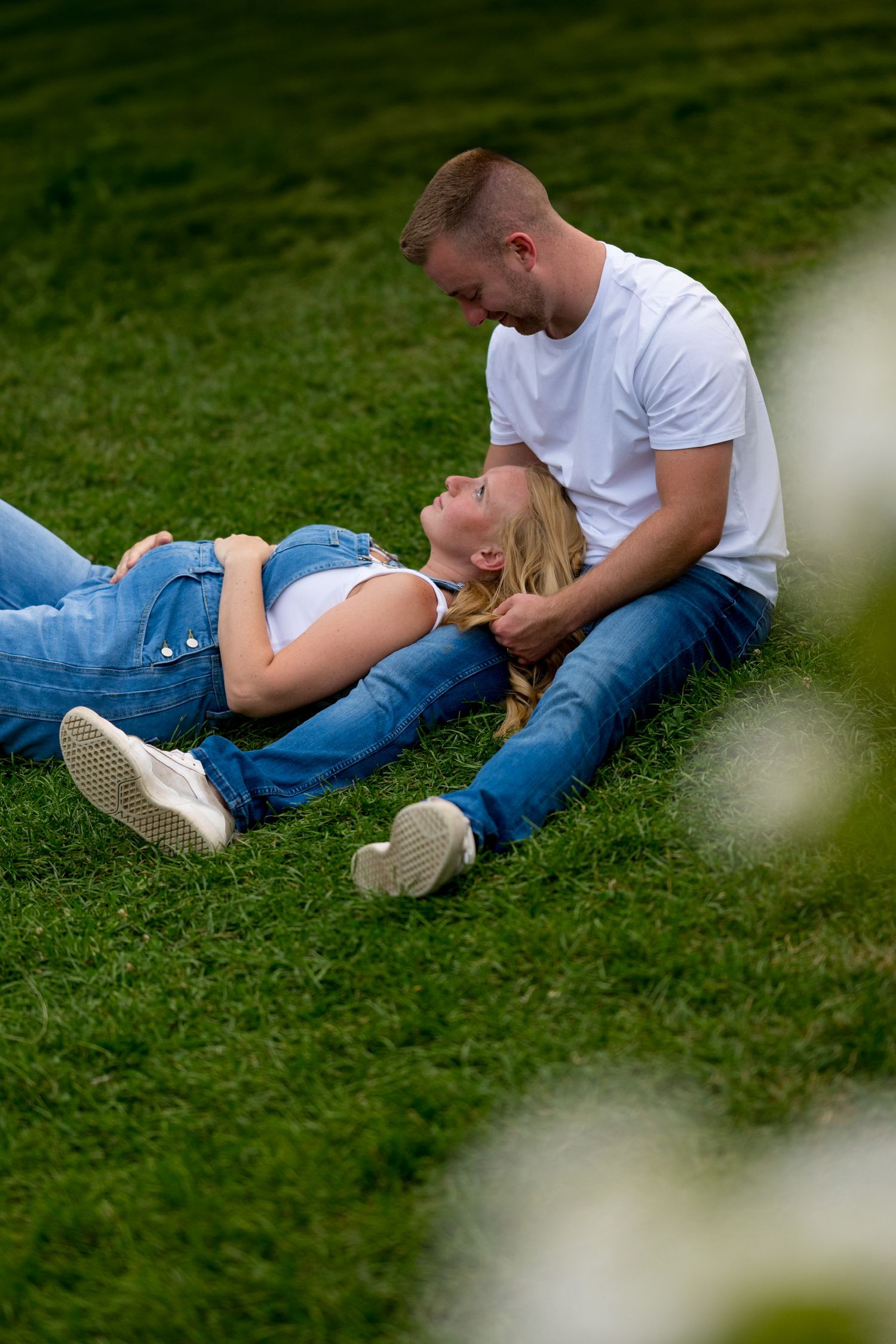 Couple lying together on green grass in casual summer attire.