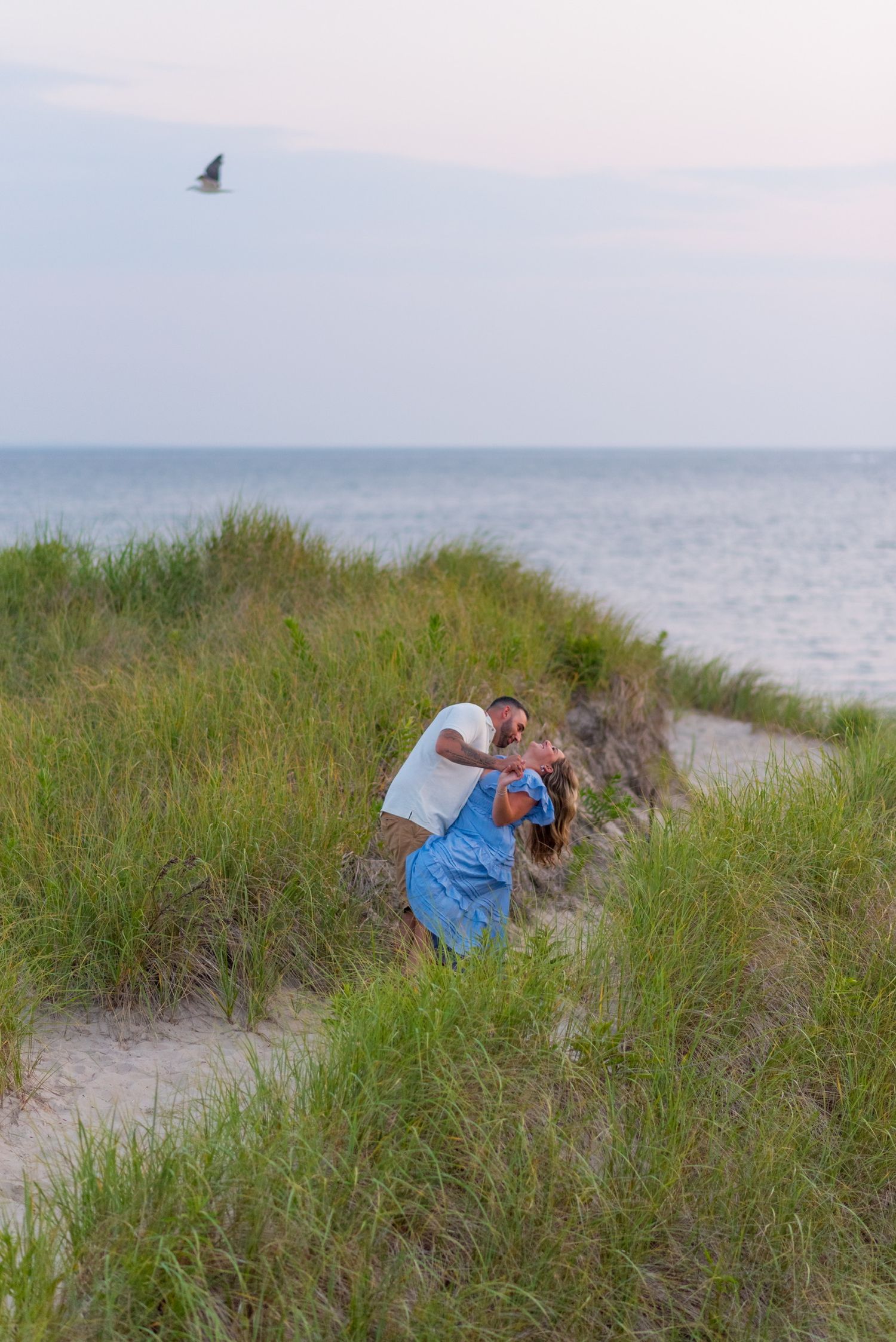 Figures exploring sand dunes and beach grass near the ocean at dusk.