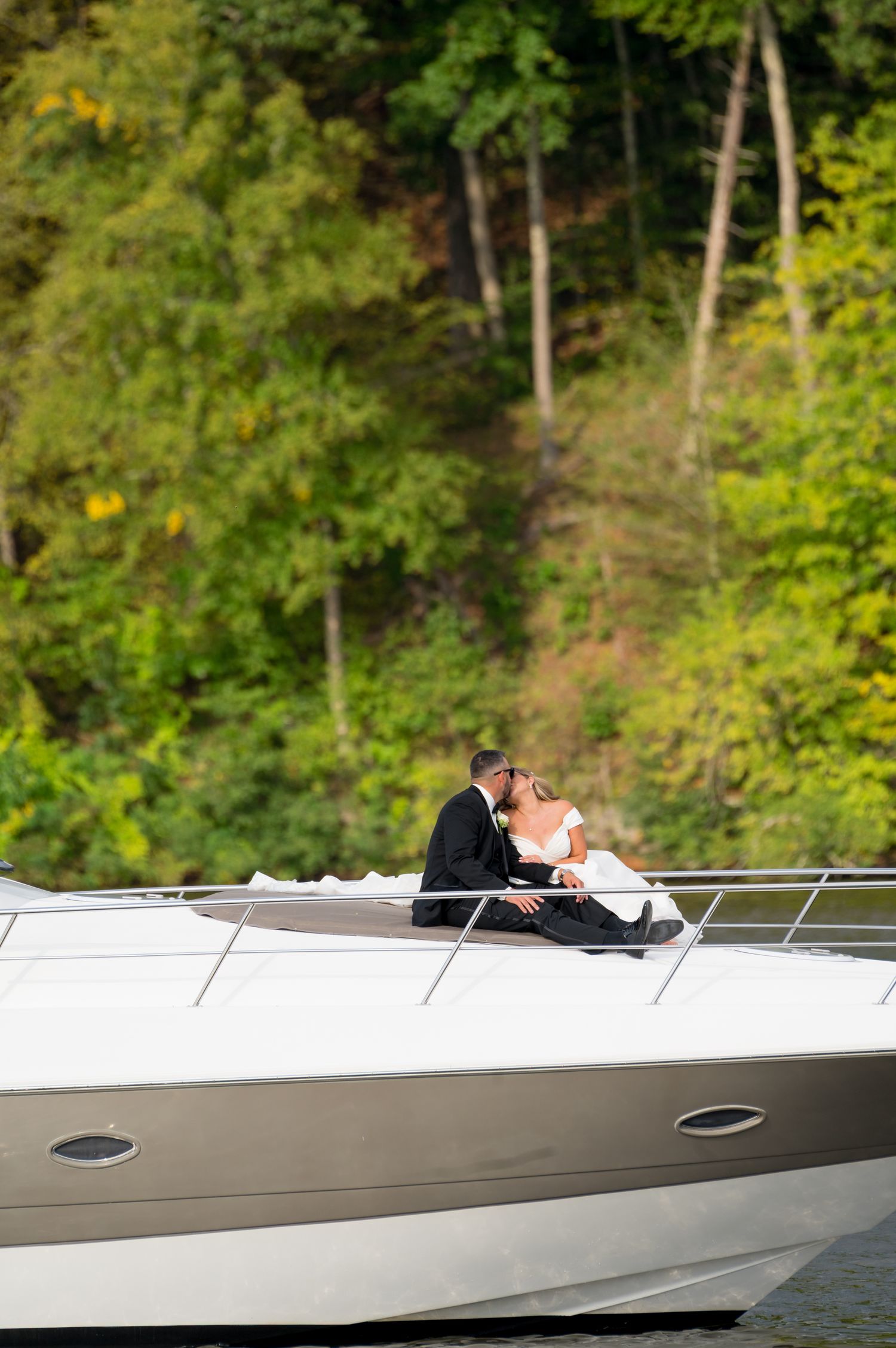 A couple shares a romantic moment on a sleek white speedboat against a lush green forest backdrop.