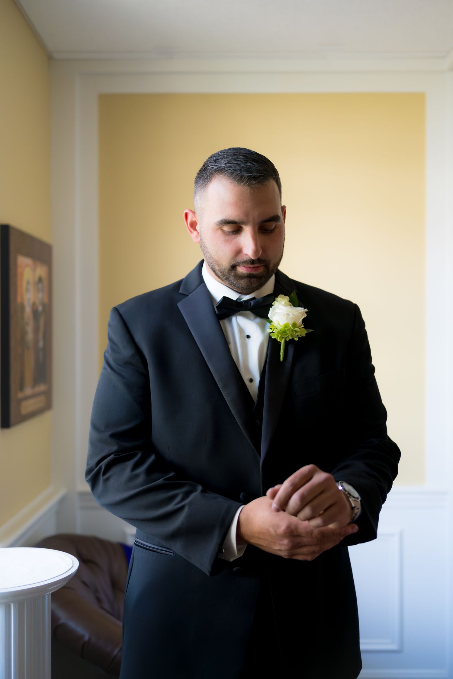 A person in a black tuxedo and bowtie adjusts their cufflinks while getting ready for a formal event.