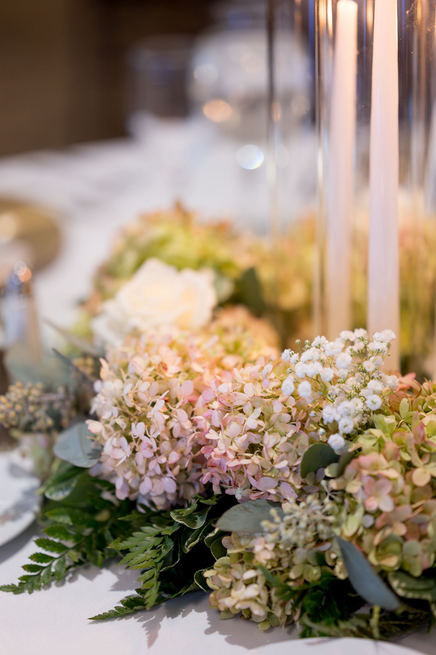 Soft pink and green hydrangea floral arrangement on white tablecloth.