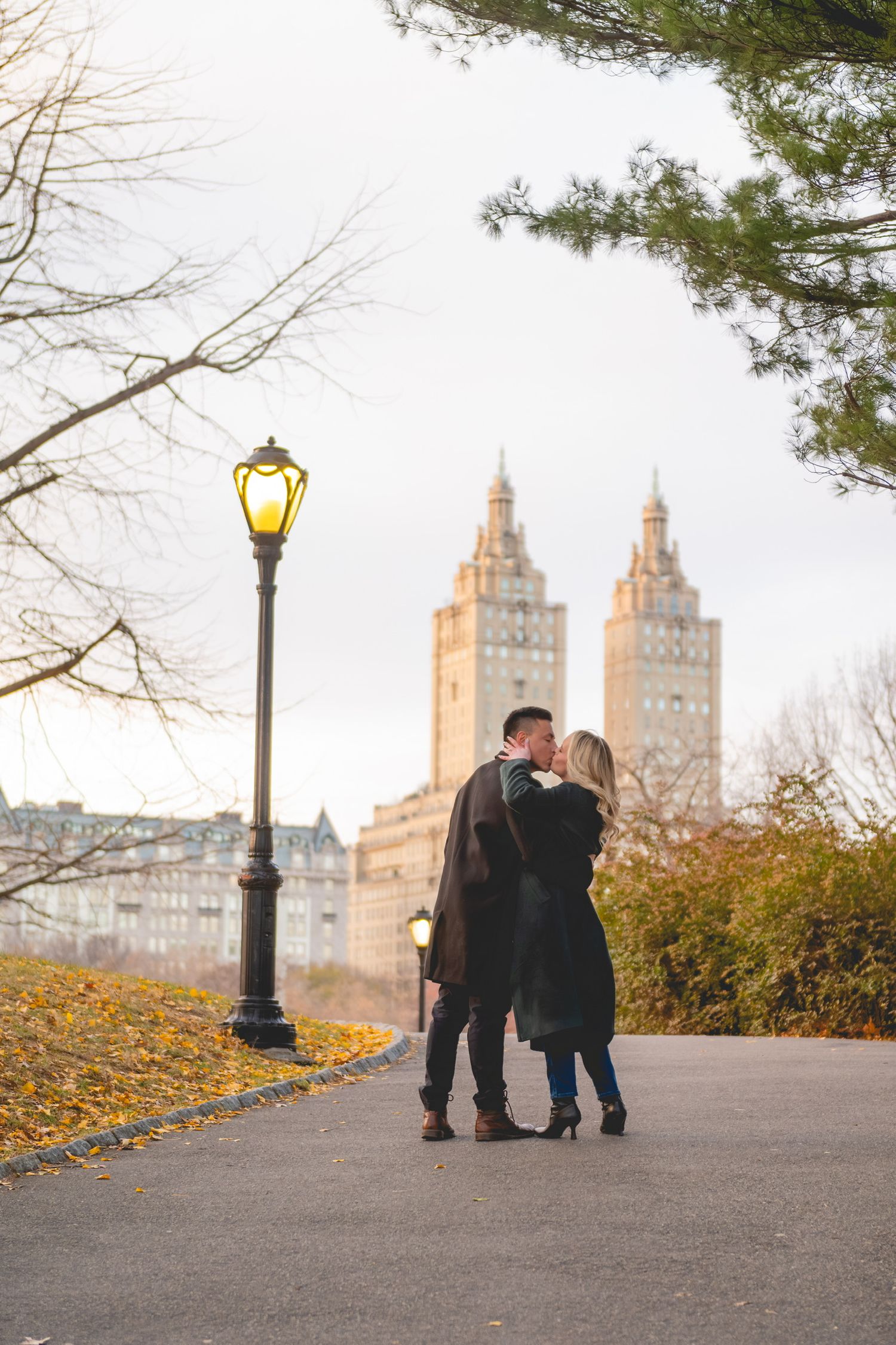 Two people walking on a path with iconic New York City buildings visible in the fall setting in Central Park.