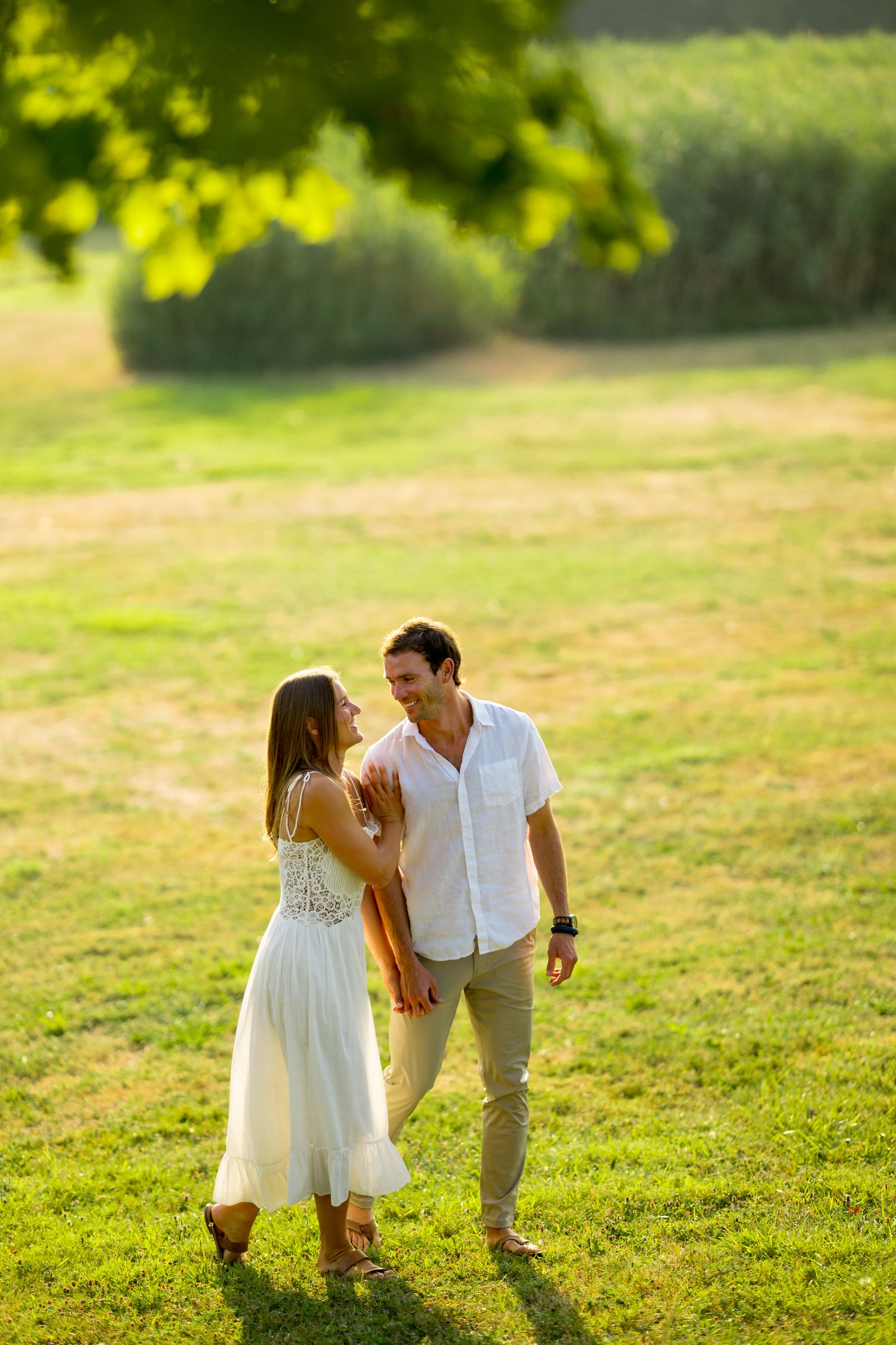 A series of romantic moments captured on a grassy hillside during golden hour showing a couple in white outfits.