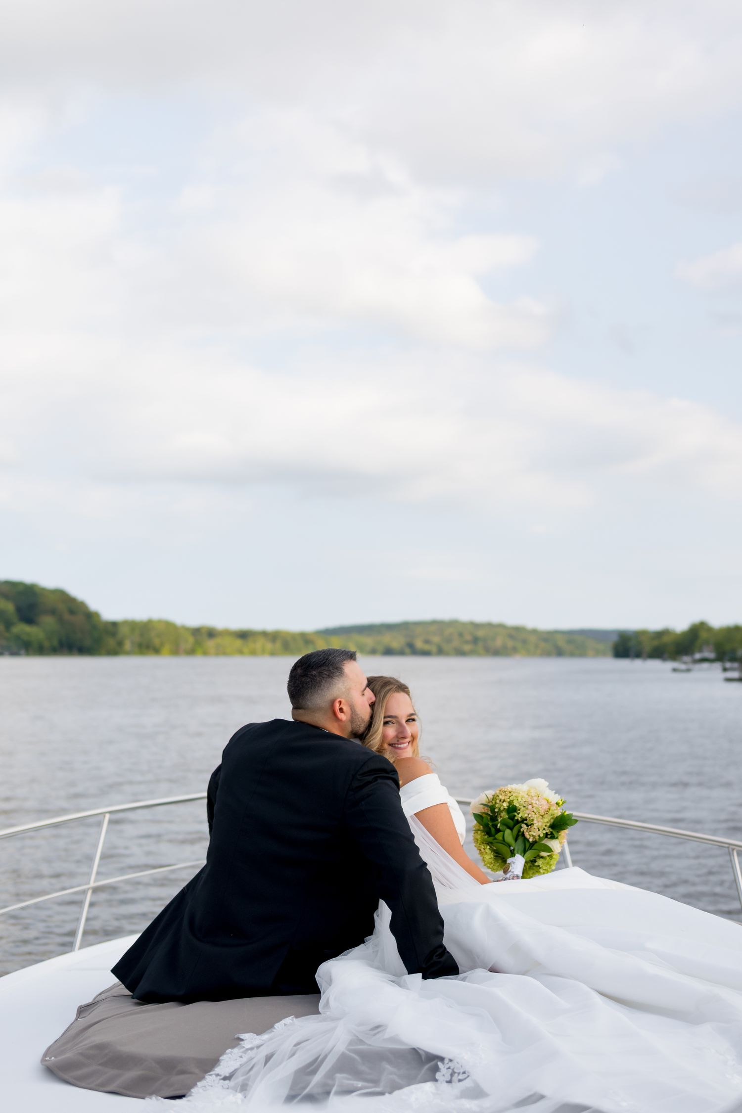 Romantic boat photoshoot with couple reclining on deck with flowing white dress against water backdrop.
