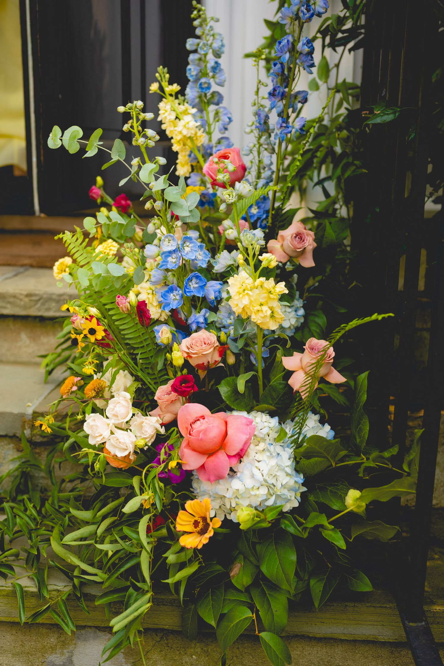 Vibrant floral arrangement with blue, pink, and yellow blooms decorates an outdoor entrance.