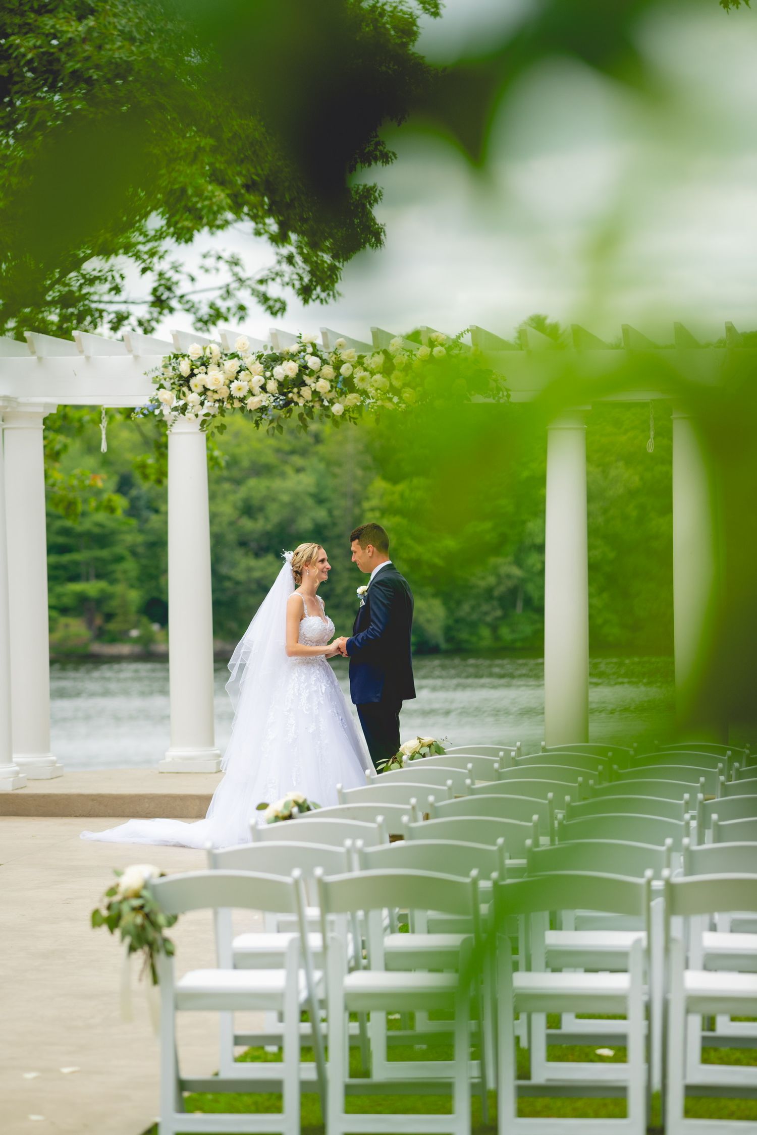 Outdoor wedding ceremony setup with white chairs and columns overlooking a lake.