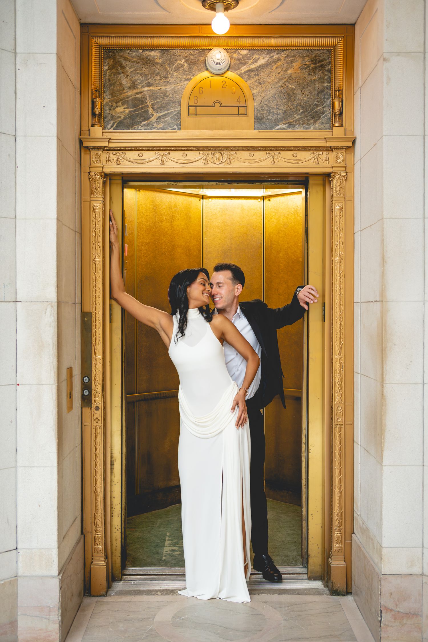 A couple poses romantically in golden-lit elevator doorways of a historic building at Hartford City Hall.
