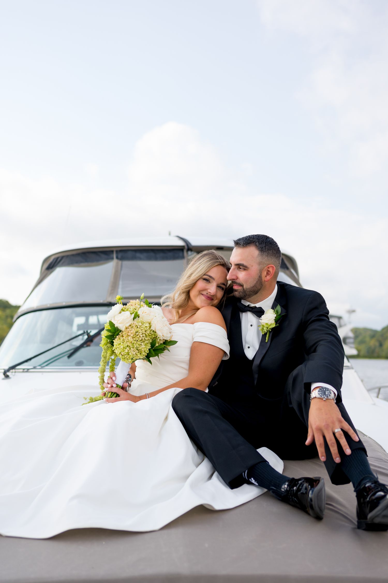 Wedding couple sitting together on boat deck against cloudy sky.