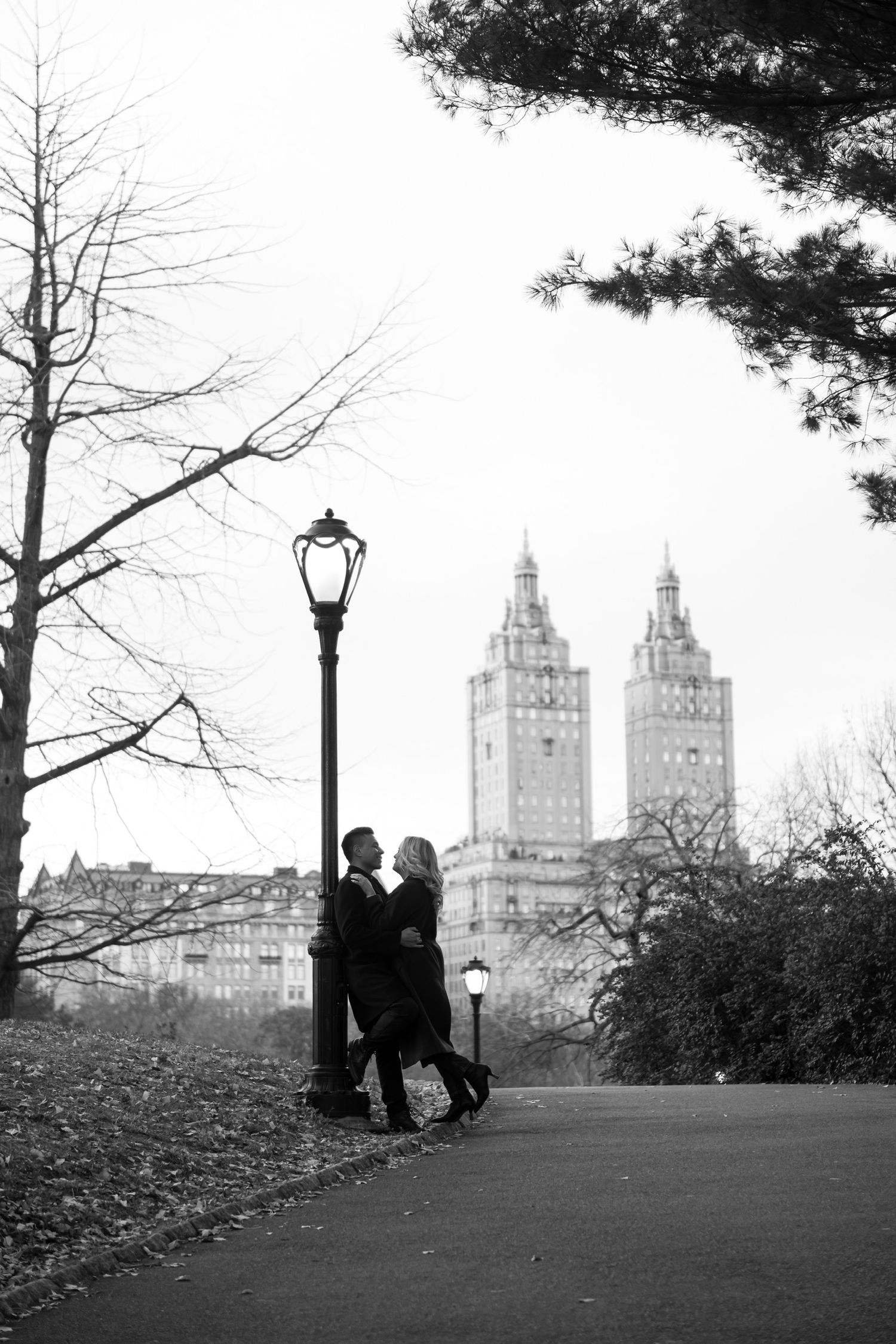 Silhouetted couple embracing near a lamppost with iconic New York City buildings in the background in Central Park in Manhattan, New York.