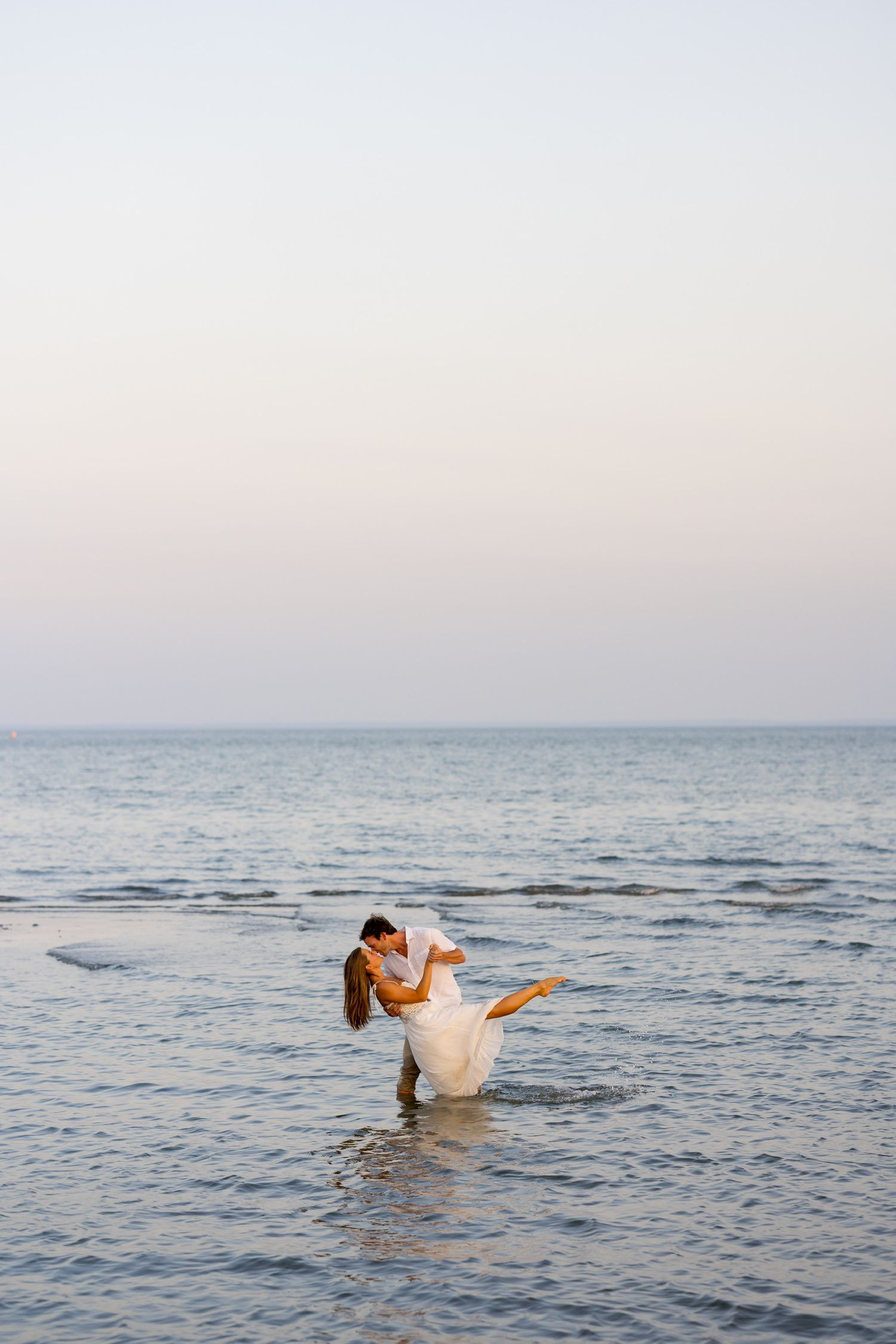 Playful couple splashing in ocean water during sunset photoshoot in Westport, Connecticut.