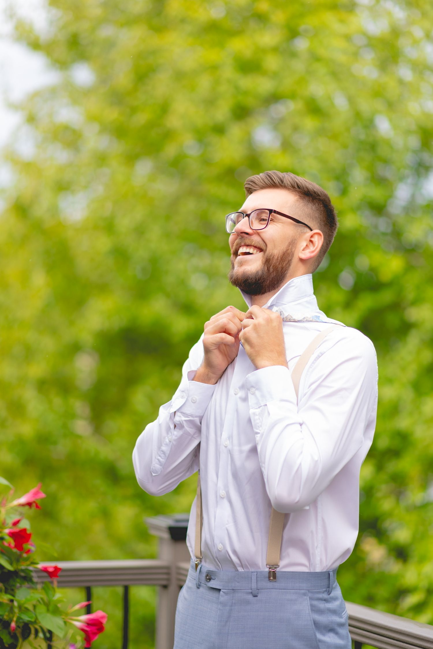 Joyful person in white shirt and suspenders laughing in garden setting.