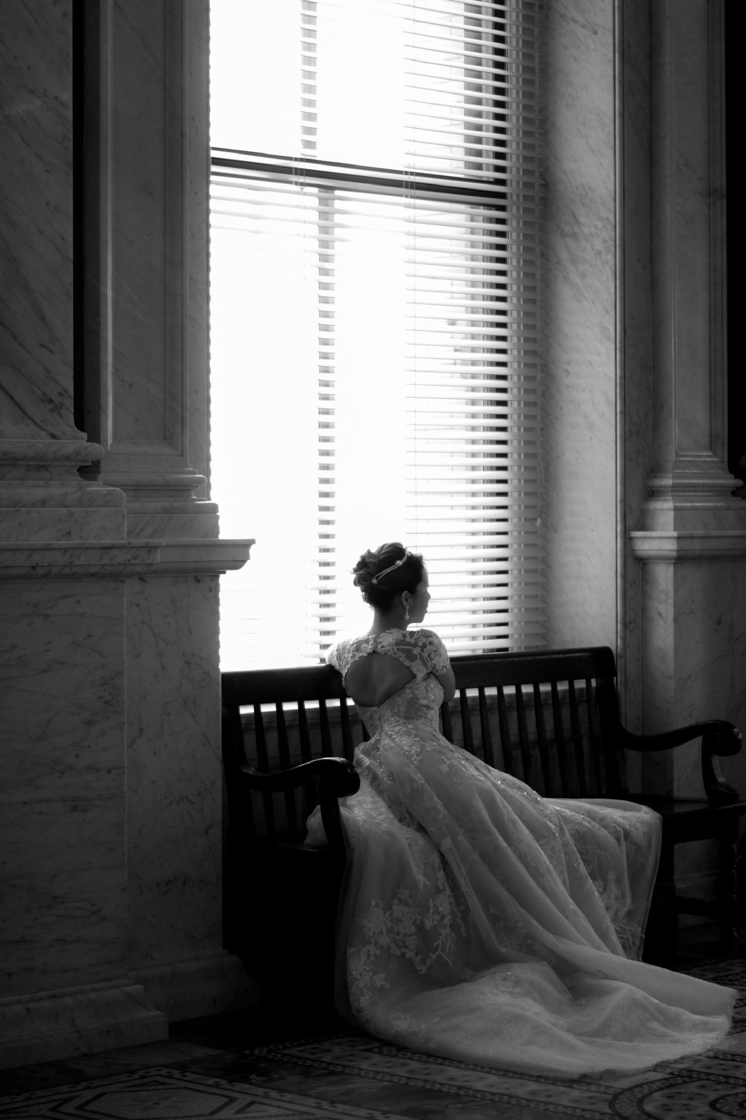Silhouette of bride in elegant dress sitting by window in black and white.