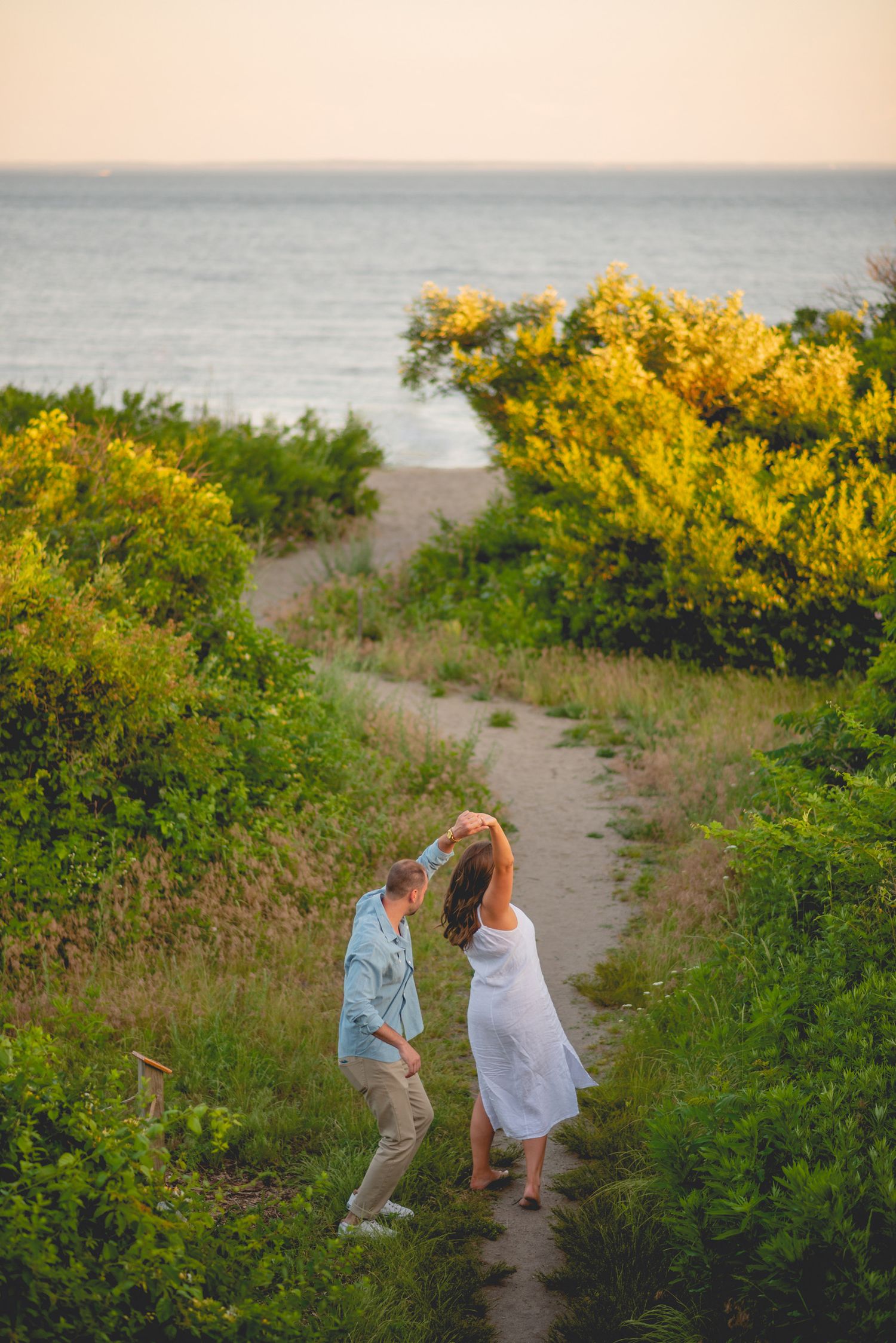 A couple walking along a coastal path lined with blooming yellow wildflowers at sunset in Connecticut.