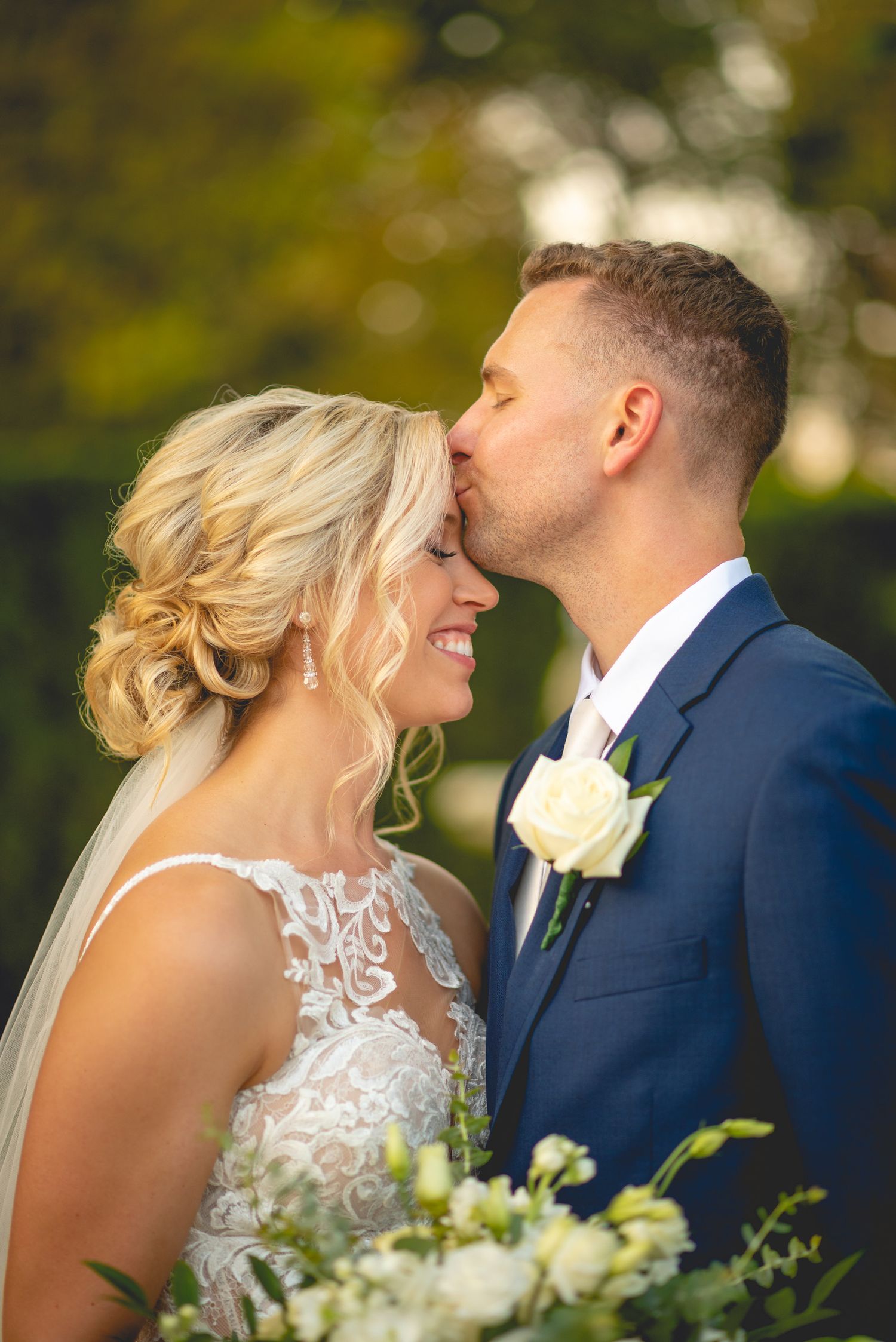 Intimate wedding portrait with white bouquet against autumn foliage background.