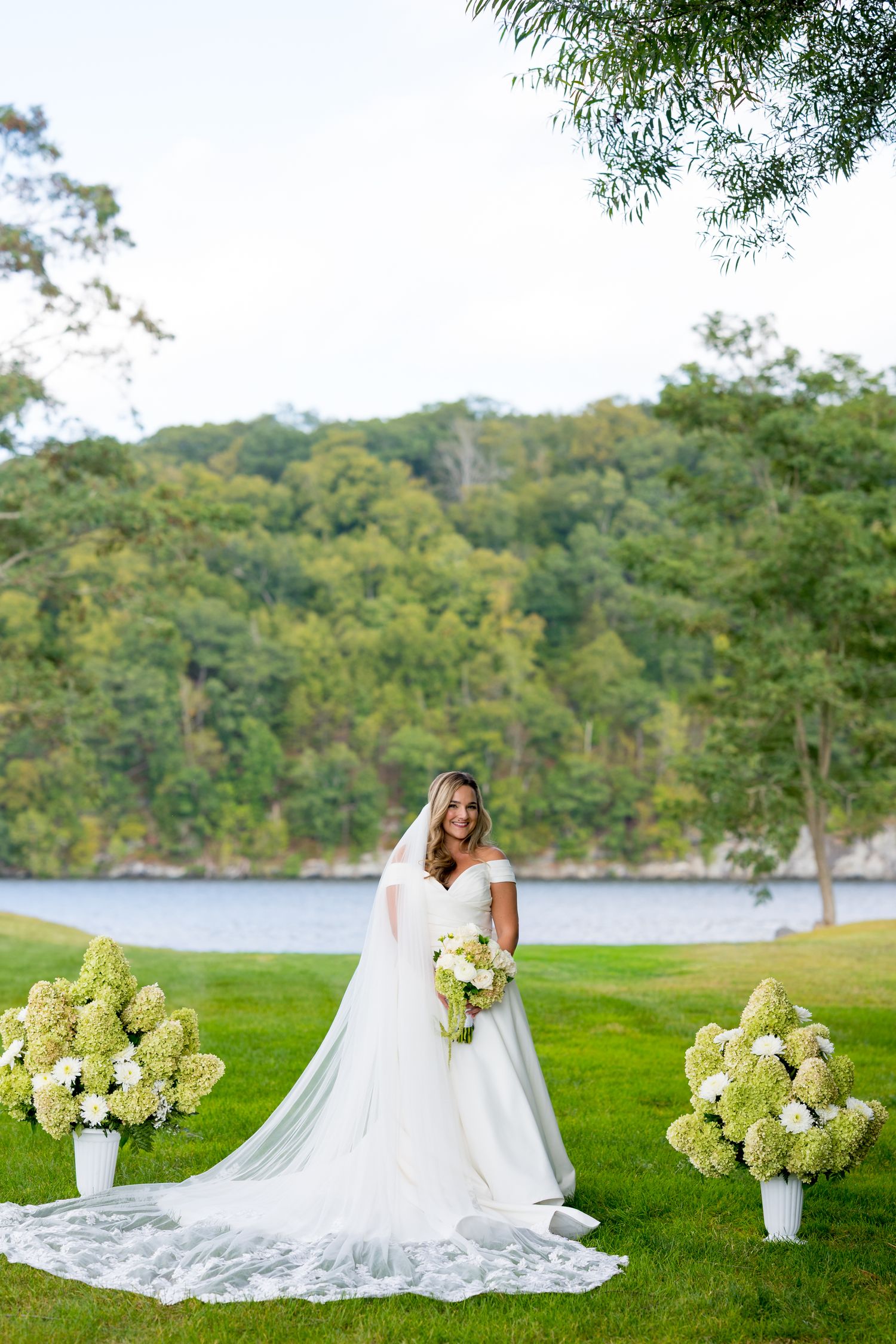 Wedding dress spread out on green lawn with waterfront and trees in background.