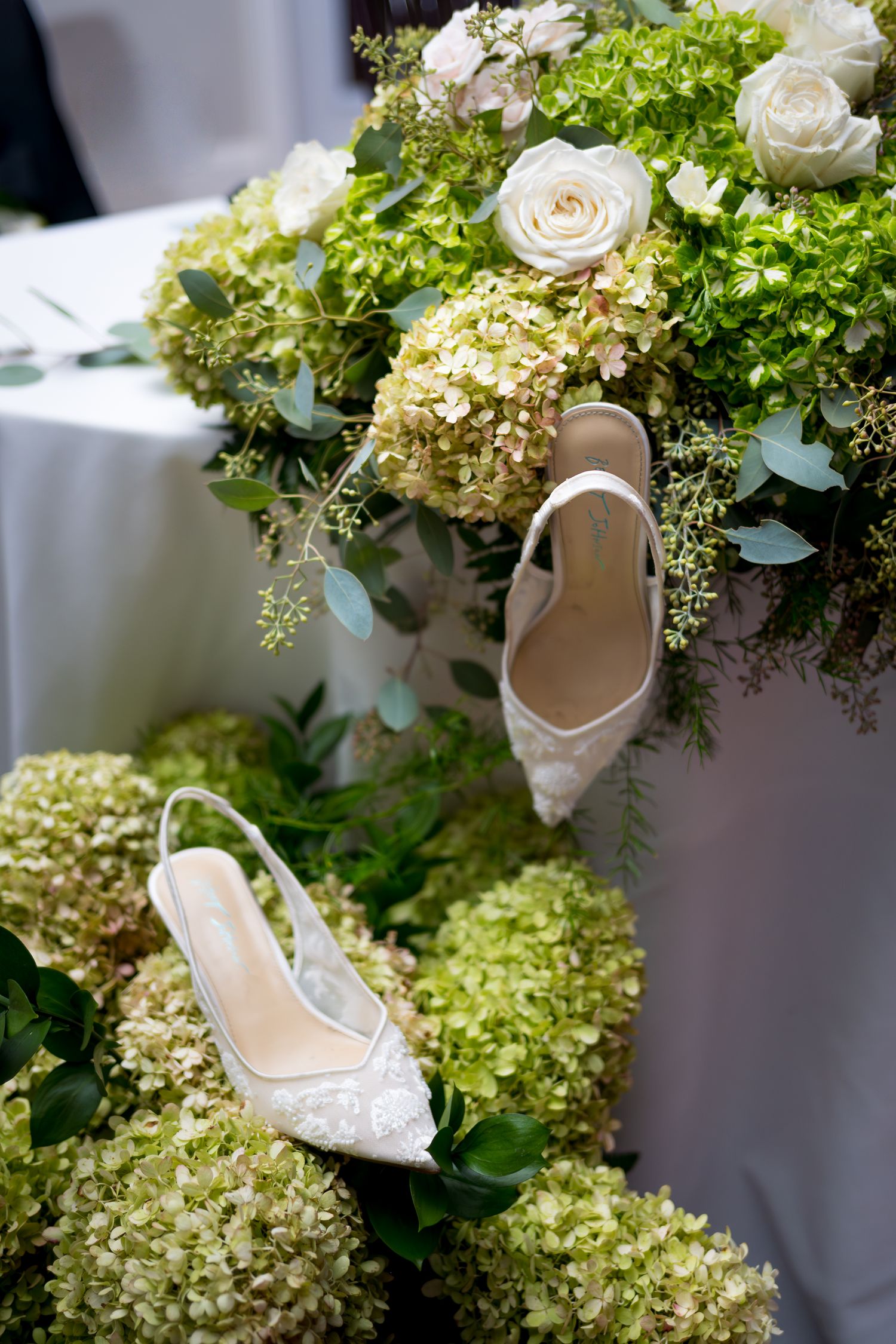 White wedding shoes nestled among lush green hydrangeas and white roses.