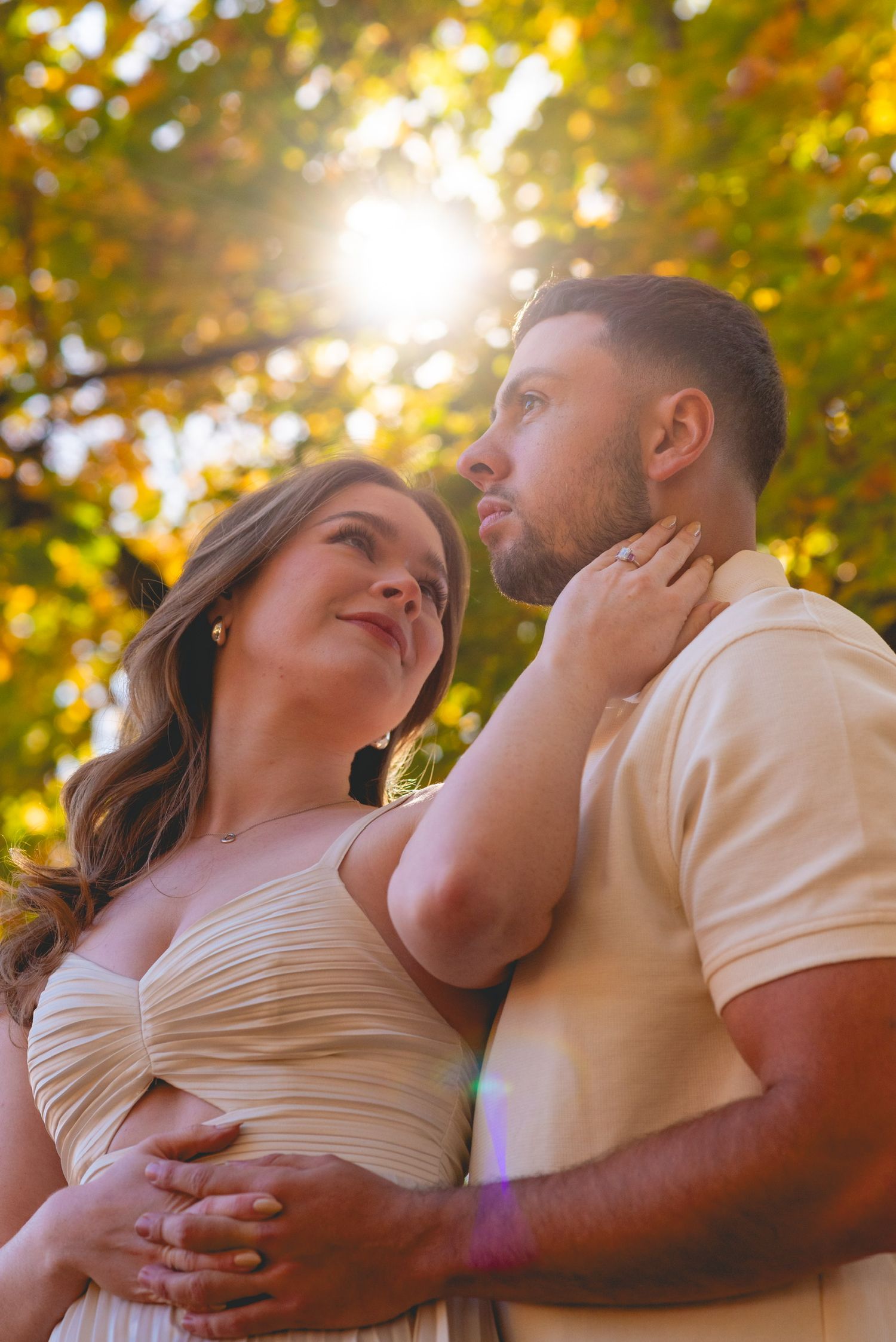 Romantic couple embraces in warm sunlight with golden bokeh and fall foliage.