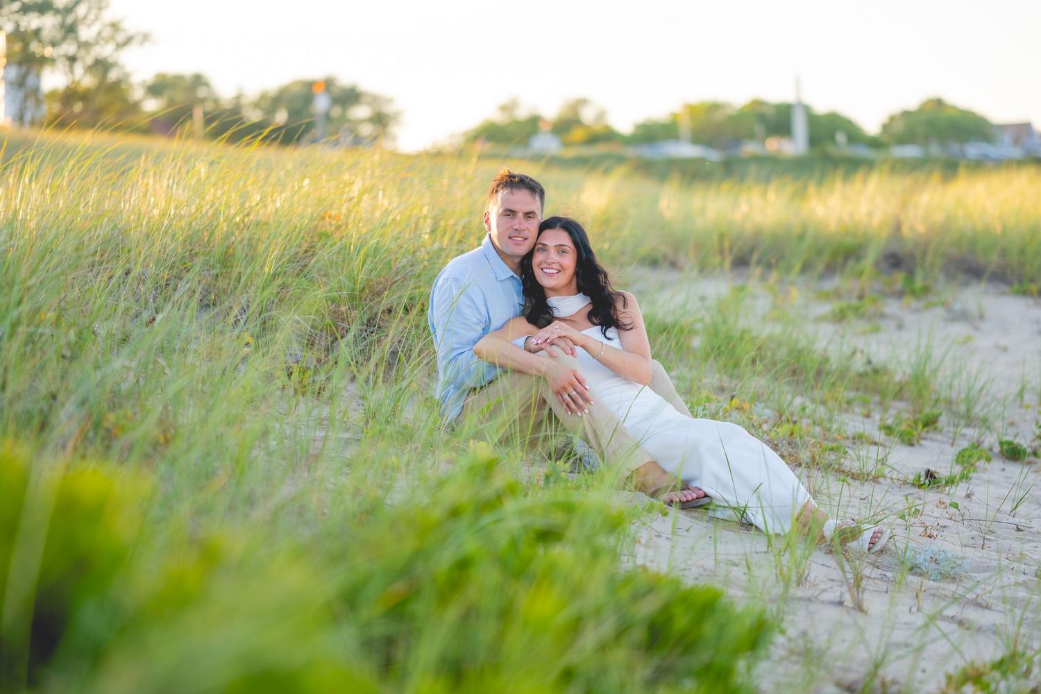 A couple sitting together in tall beach grass during golden hour at Chatham Lighthouse Beach in Chatham, Massachusetts