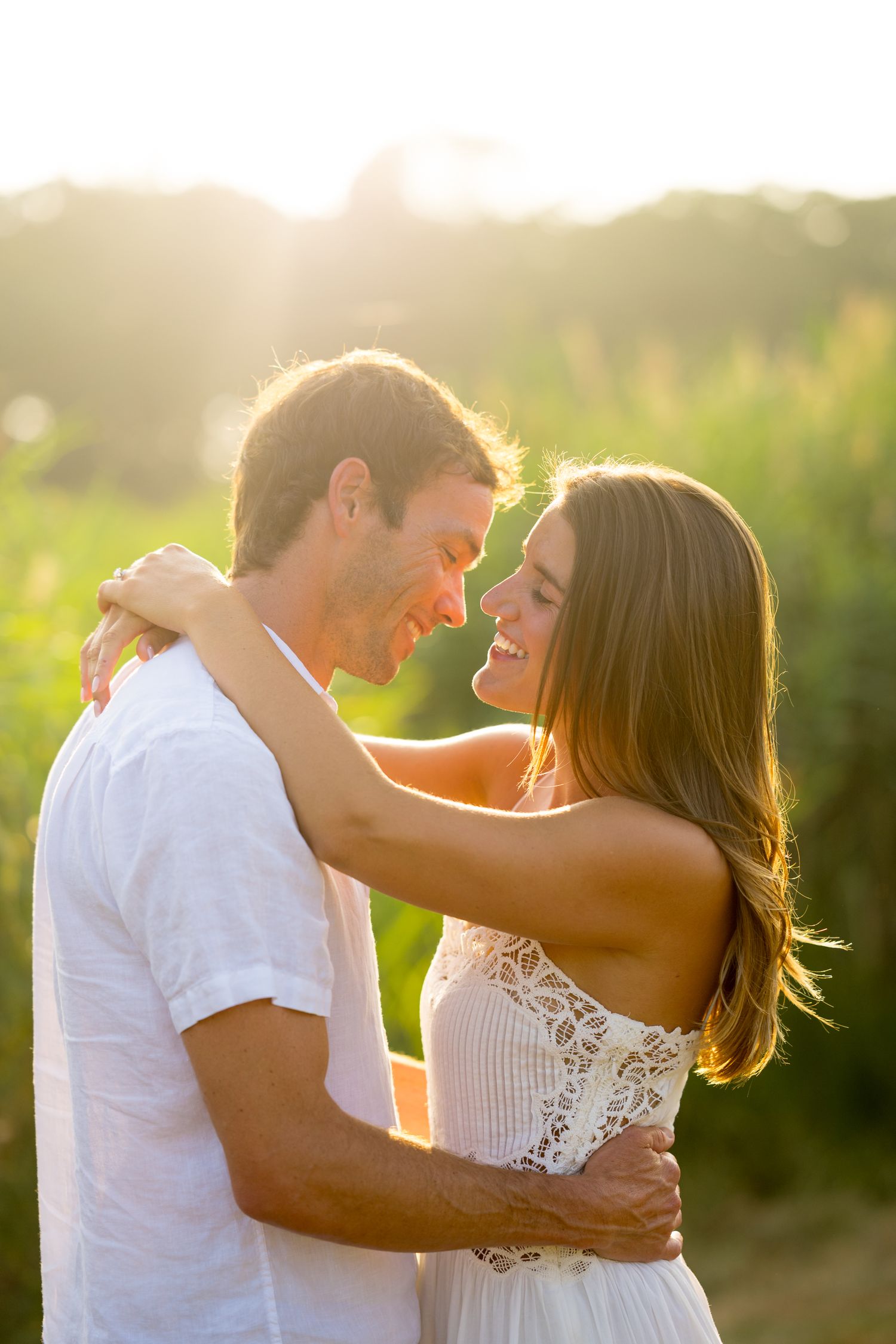 A couple embraces in a romantic moment at sunset with golden light streaming through their silhouettes.