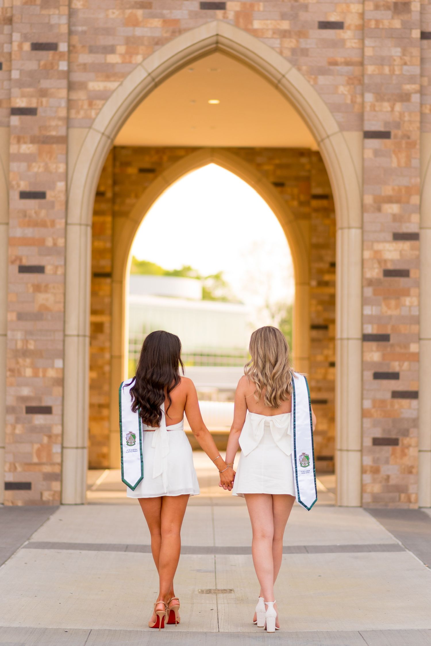 Group of women in matching white dresses walking through brick archways.