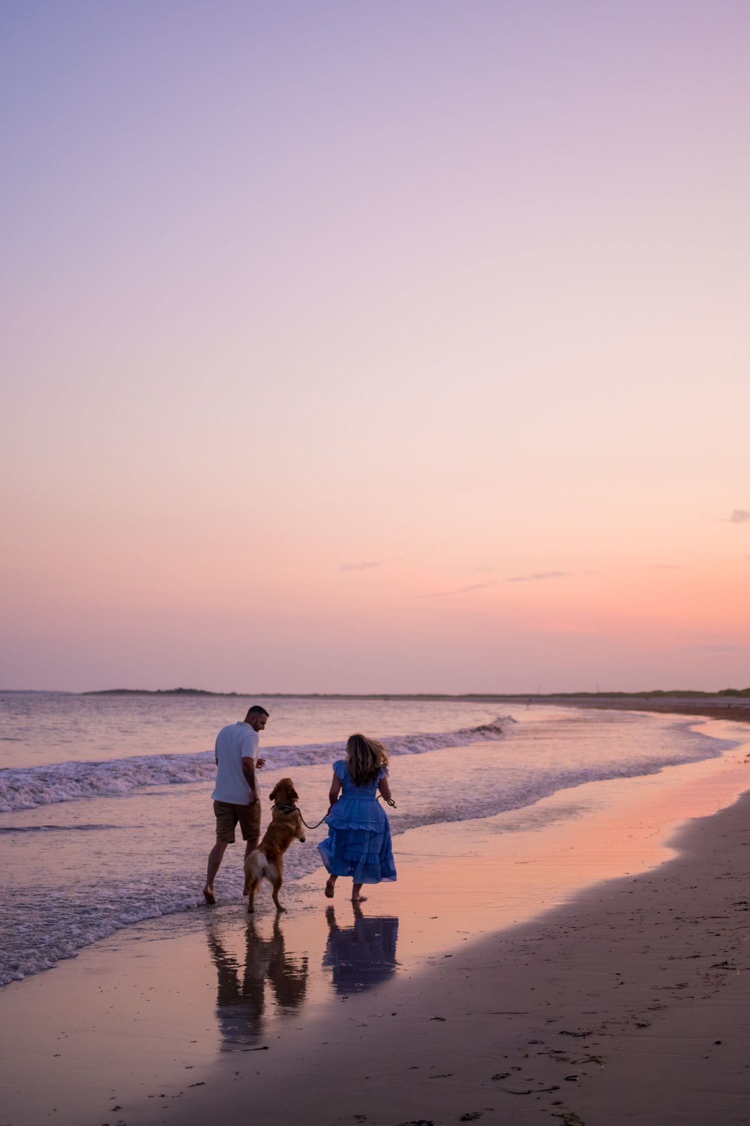 Family walking along beach shoreline during pink sunset.