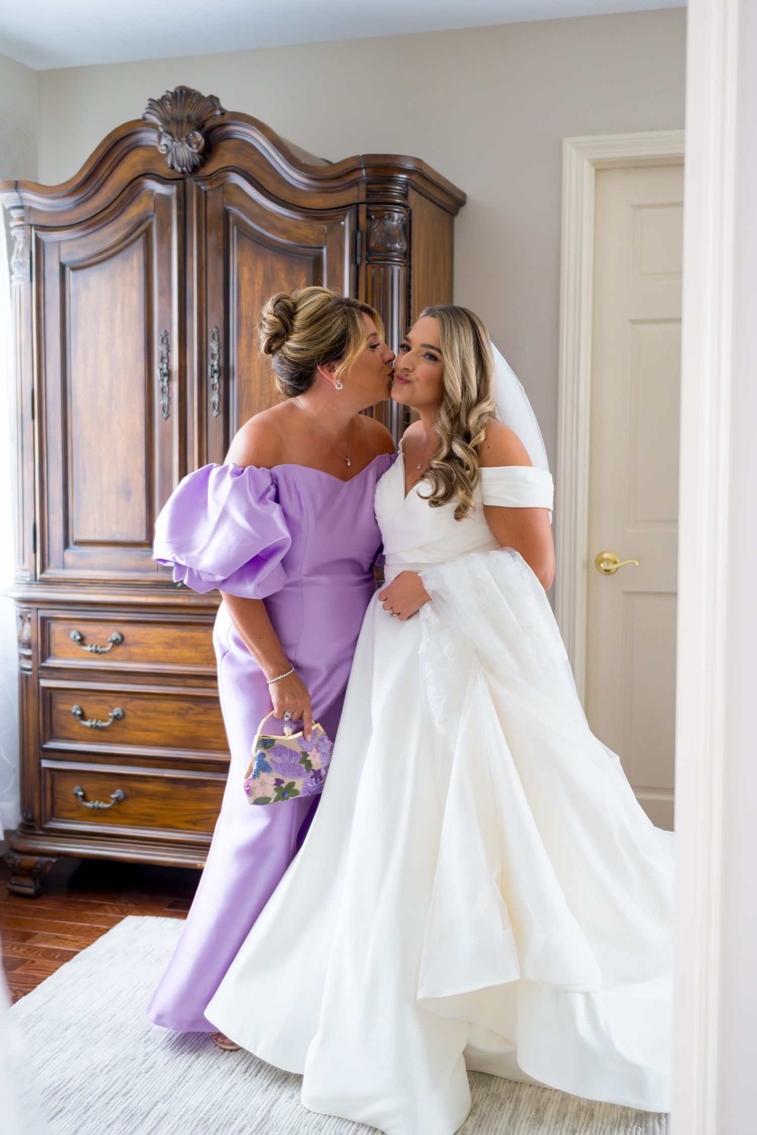 Bride in white wedding gown sharing a moment with bridesmaid in purple dress.