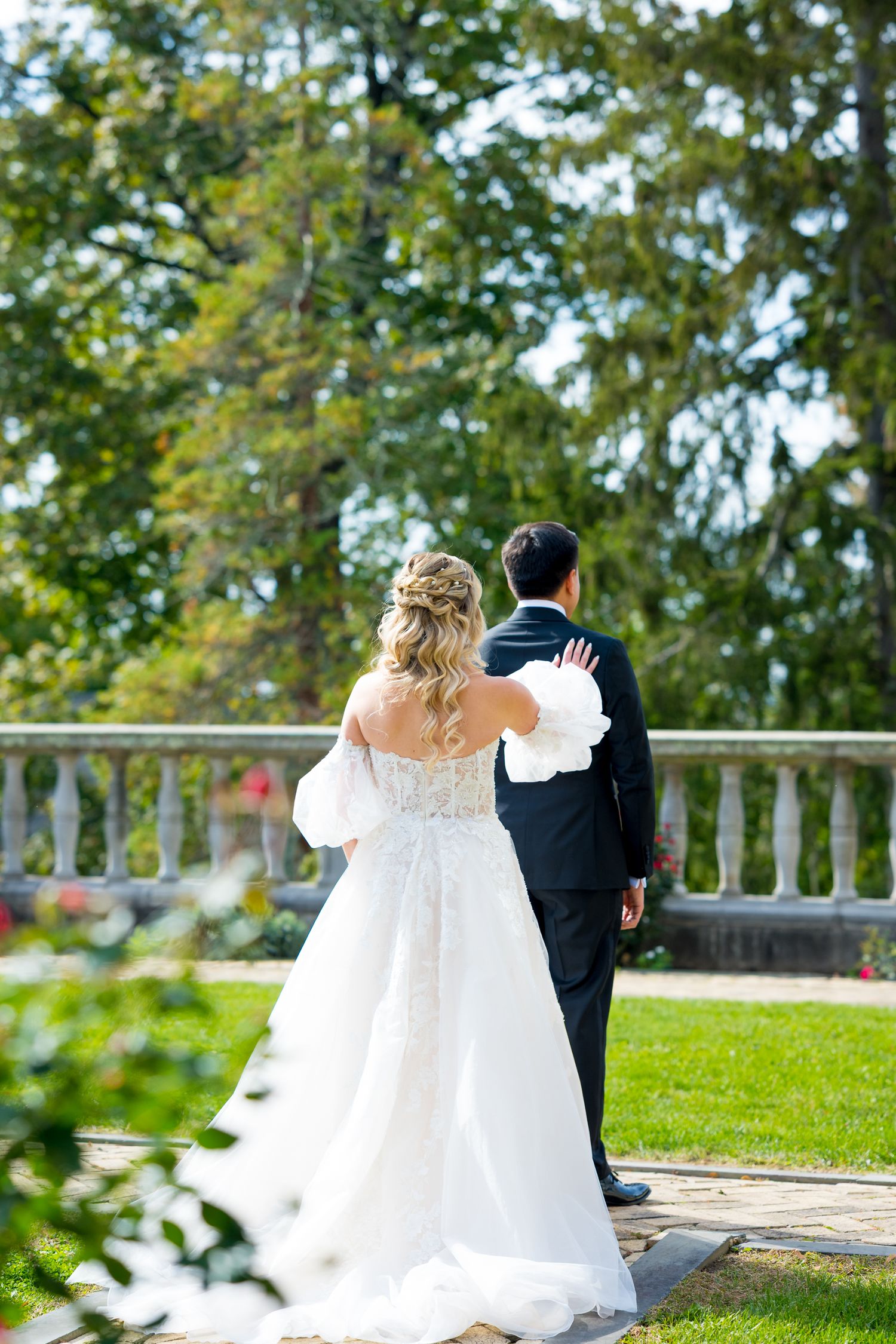 Newlywed couple sits together on stone balcony overlooking scenic garden landscape on their wedding day.