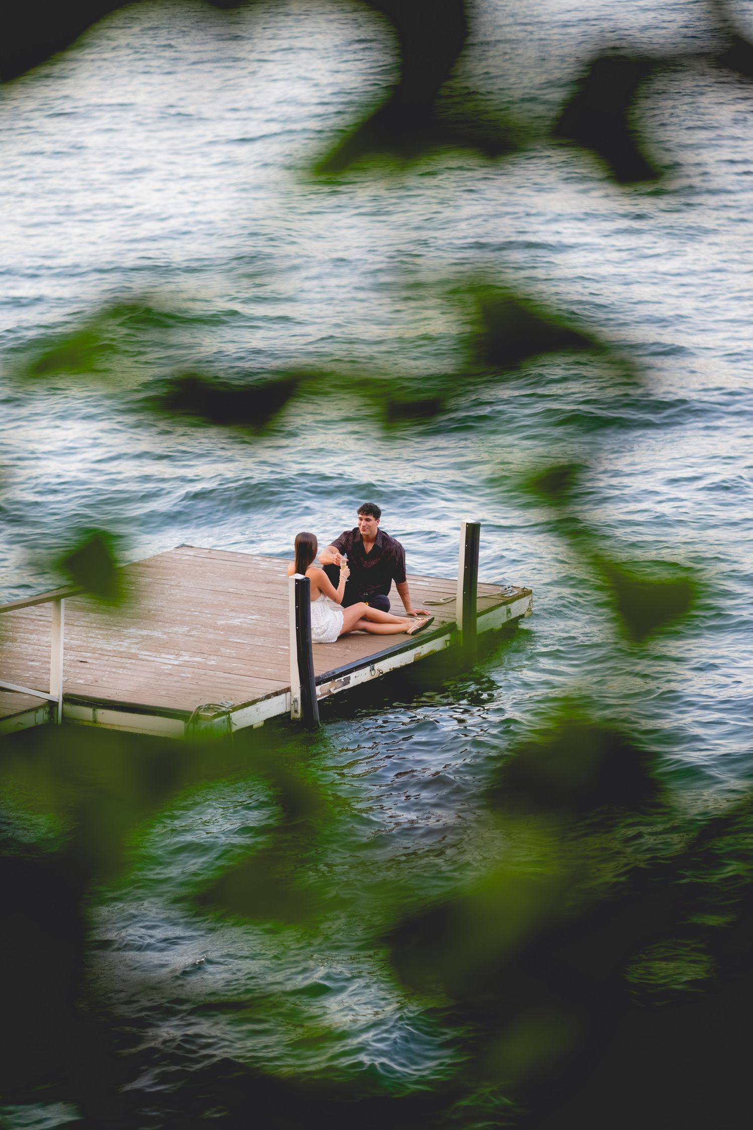 Couple sitting together on a wooden dock surrounded by water and leaves on Candlewood Lake in Connecticut.
