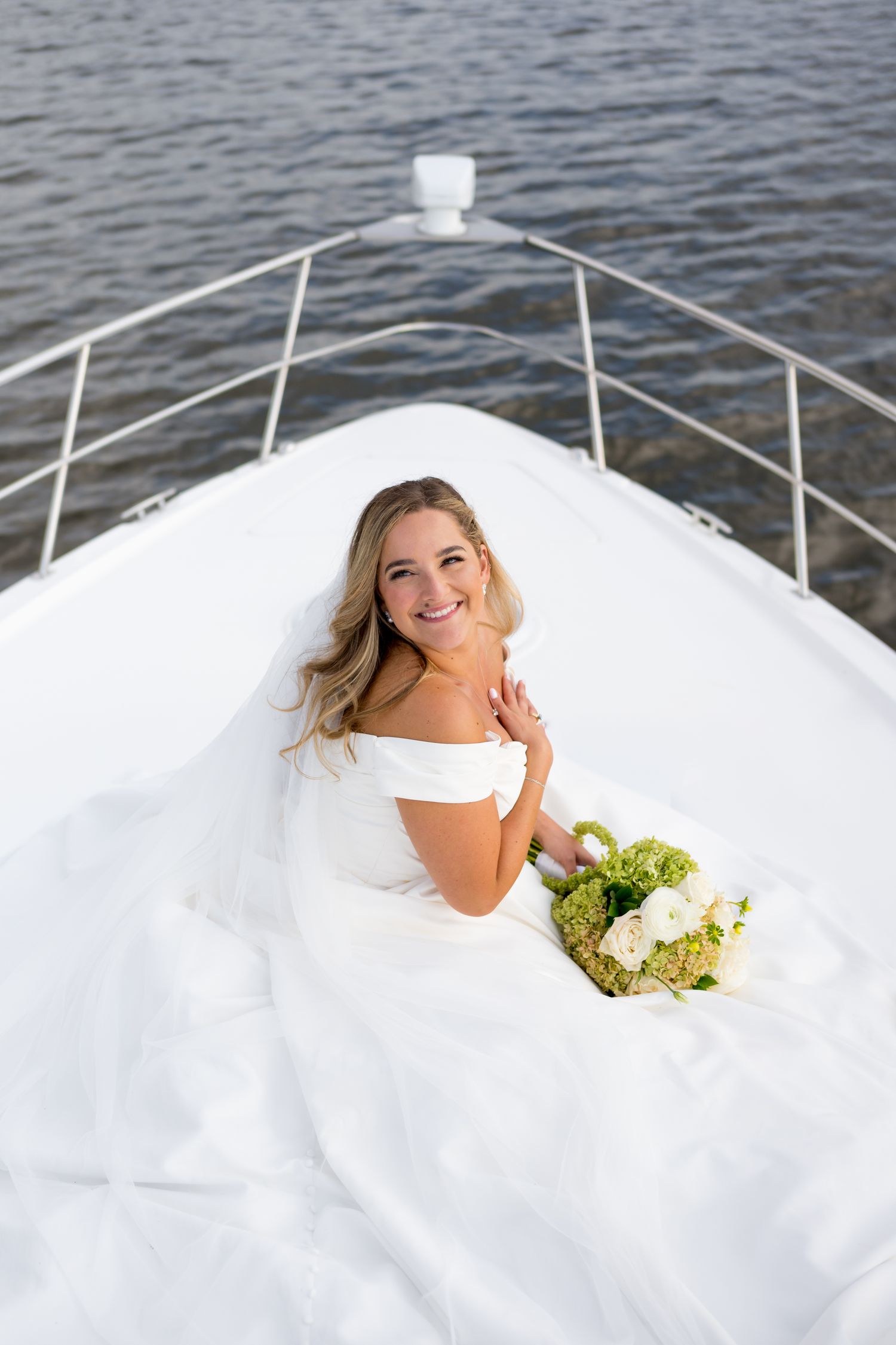 Bride in white dress poses on bow of boat holding bouquet in Connecticut.