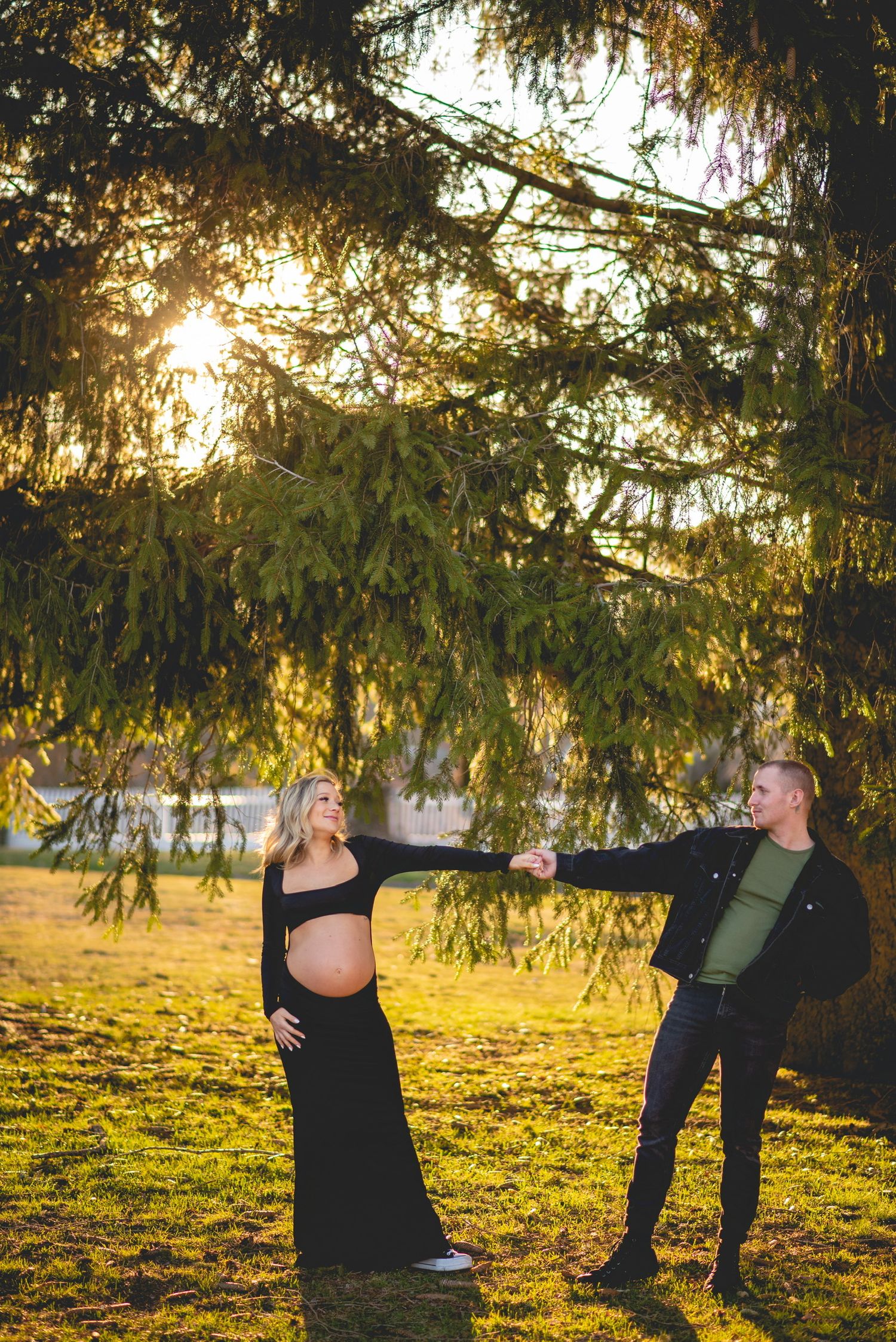 A maternity photoshoot in a golden field at sunset with dramatic lighting.