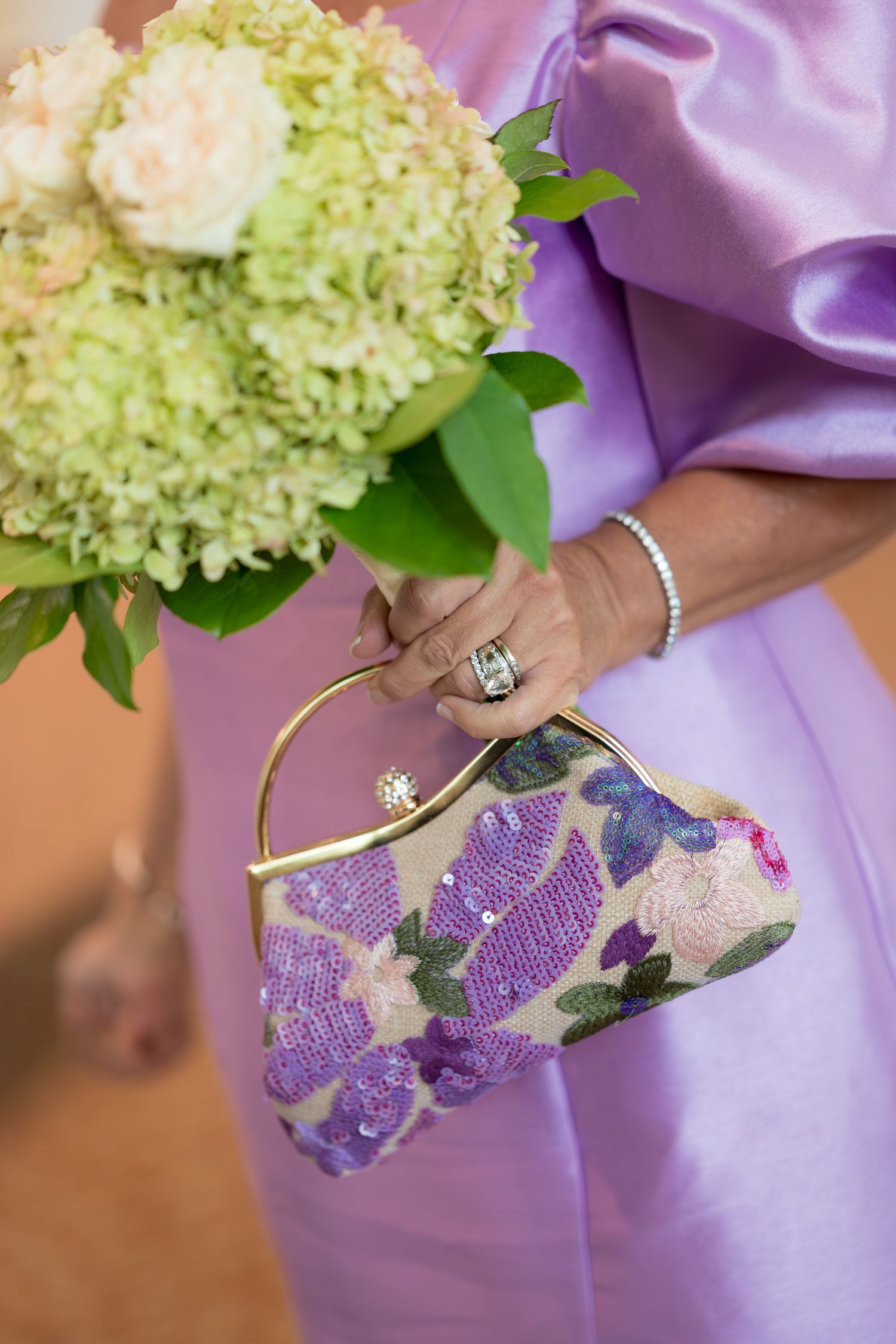 Purple gloved hands hold a white hydrangea bouquet against a lavender satin backdrop.