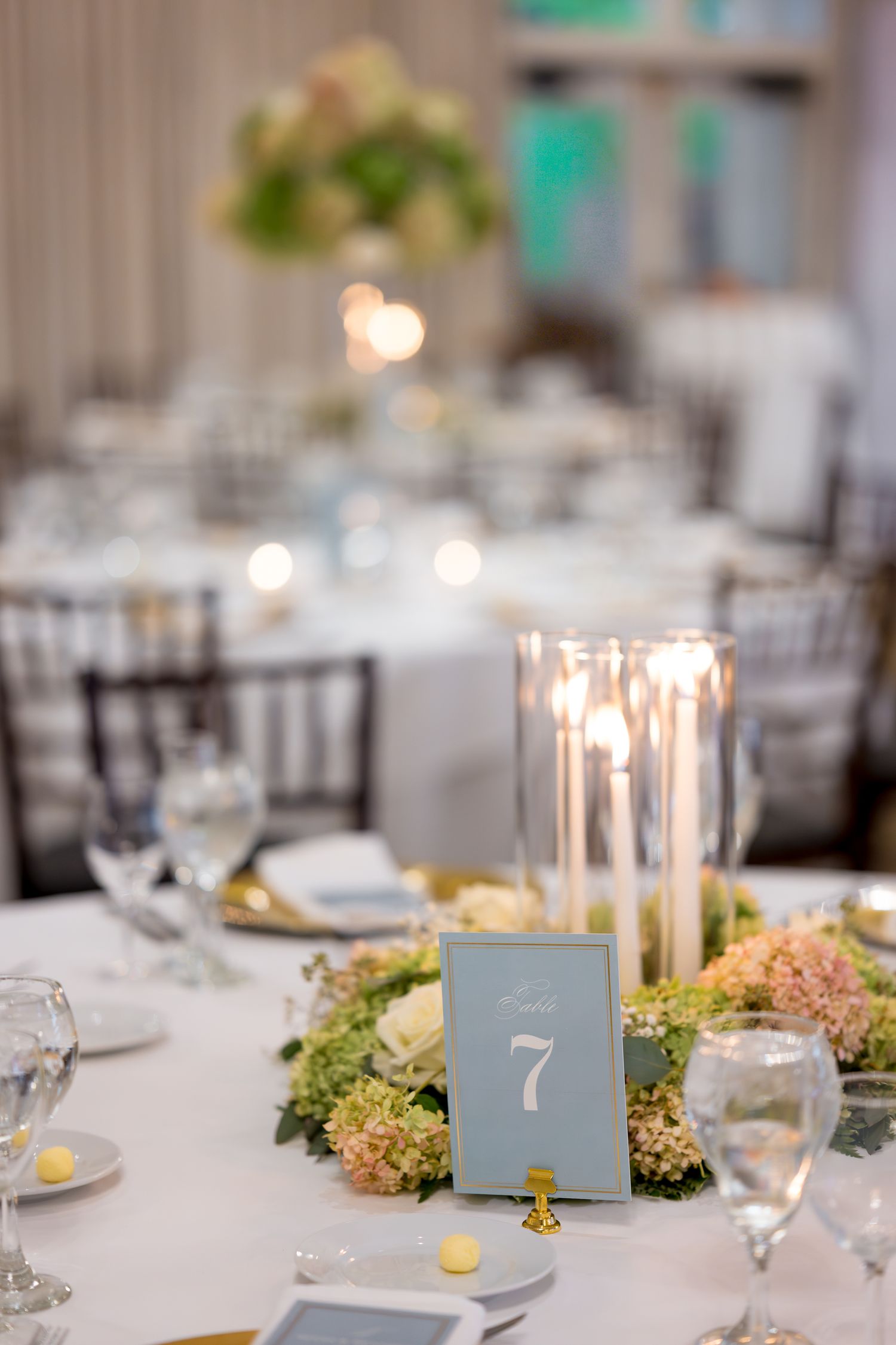 Elegant wedding reception table setting with candles, table numbers and greenery centerpieces.
